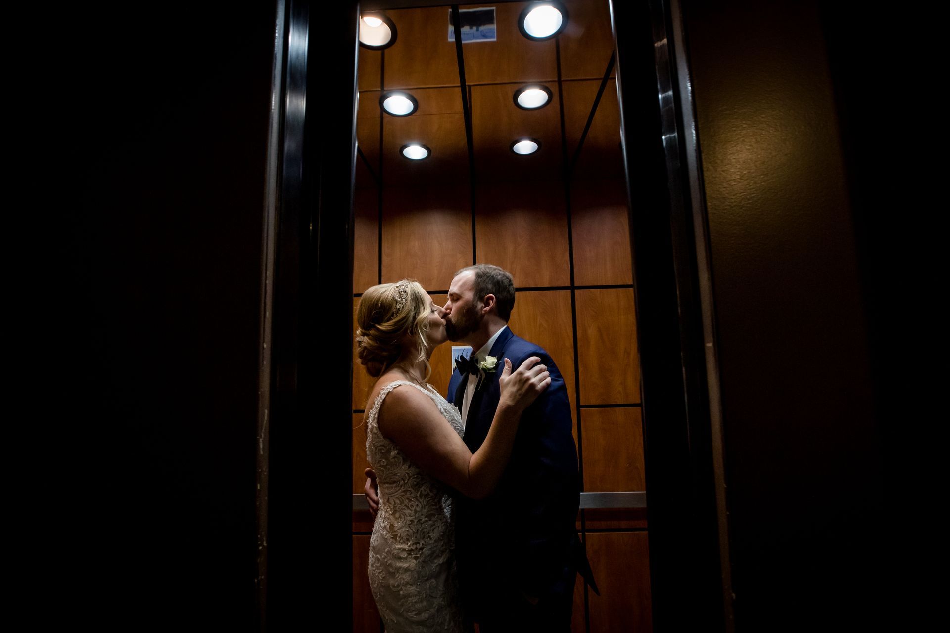 Couple in formal attire embracing in a warmly lit elevator at night