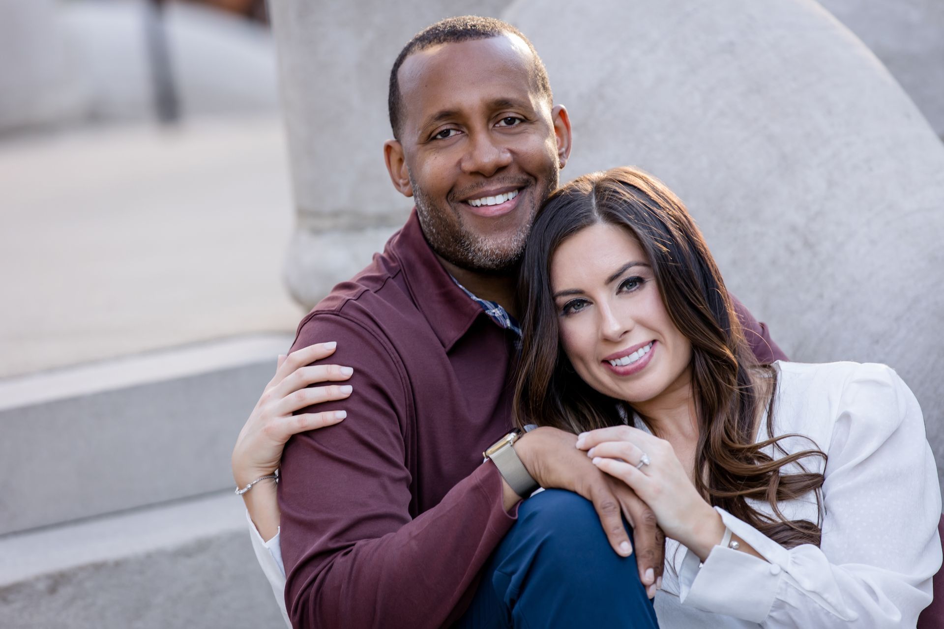 Two people smiling outdoors, leaning together on stone steps.