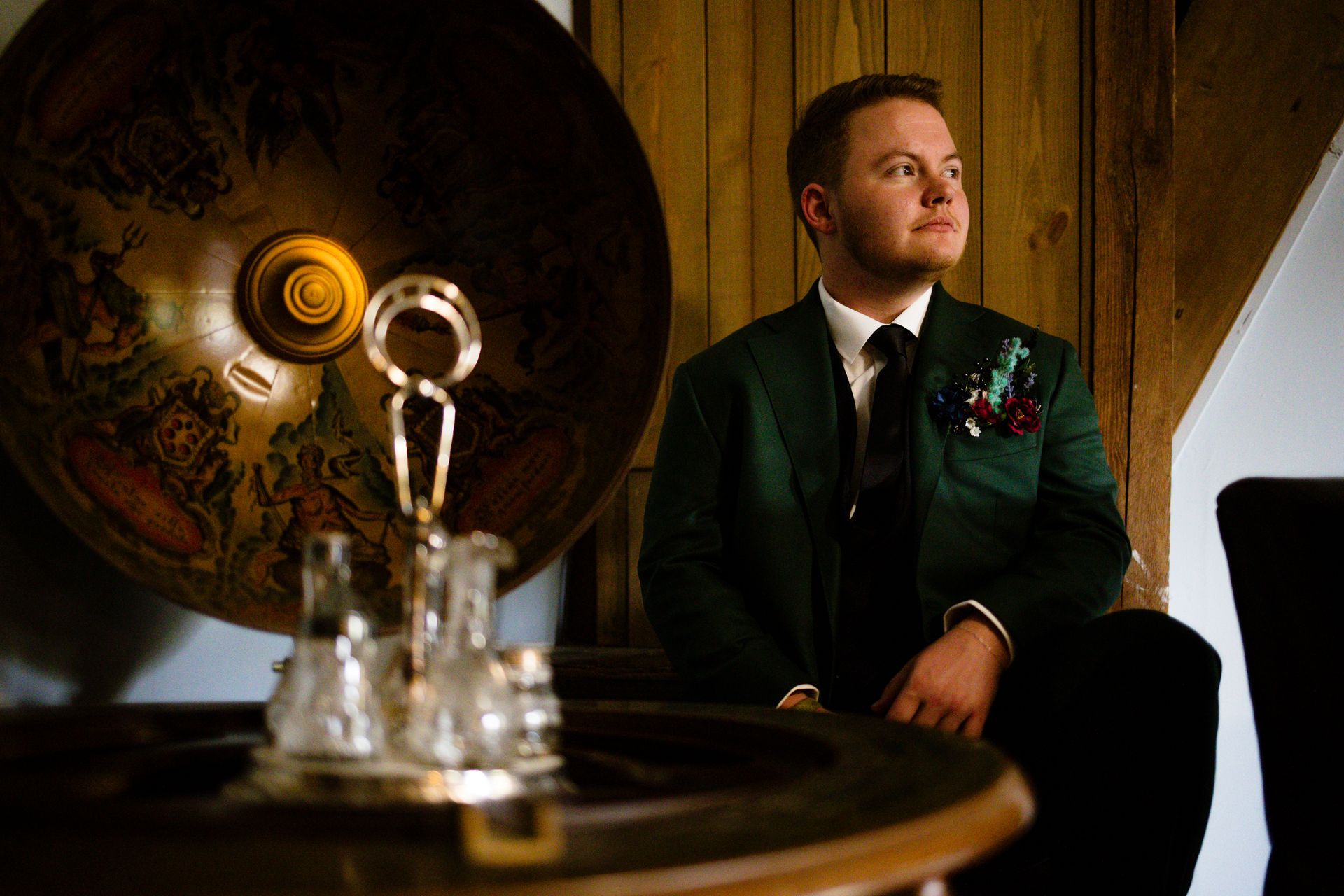 Man in dark suit seated beside a large brass gramophone in a wood-paneled room