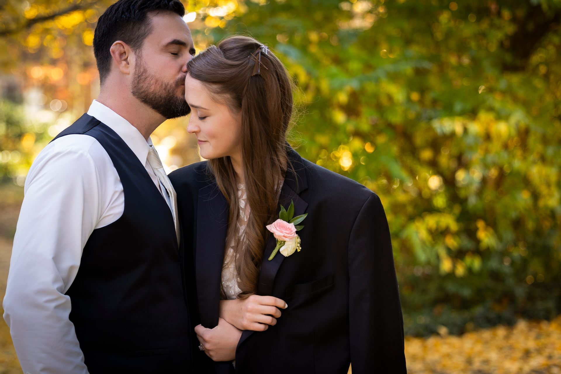 Couple embracing outdoors in fall, dressed in black, with warm golden leaves in the background