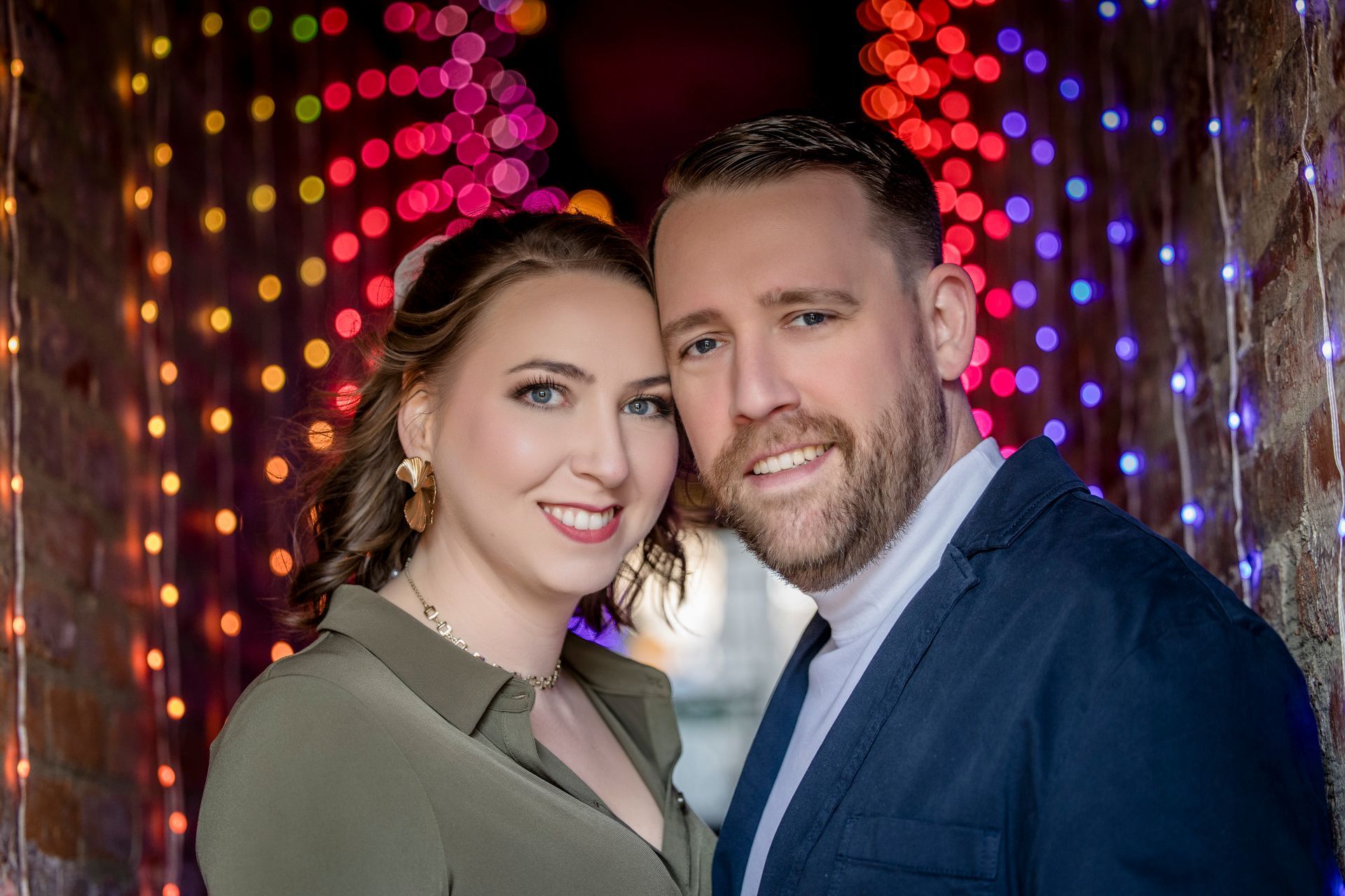 Smiling couple posing before colorful string lights at night