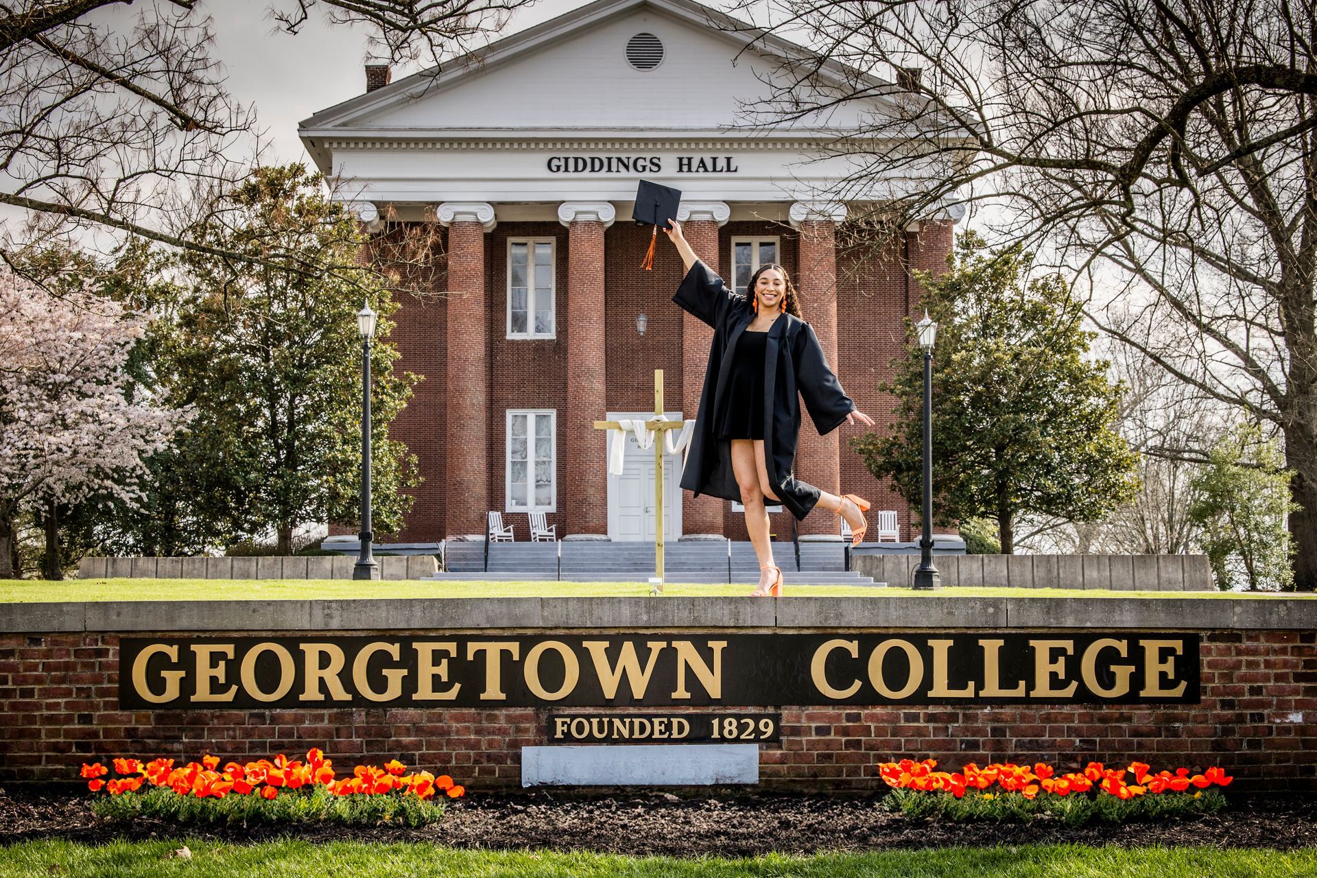Two people posing in front of Georgetown College sign and brick building in springtime