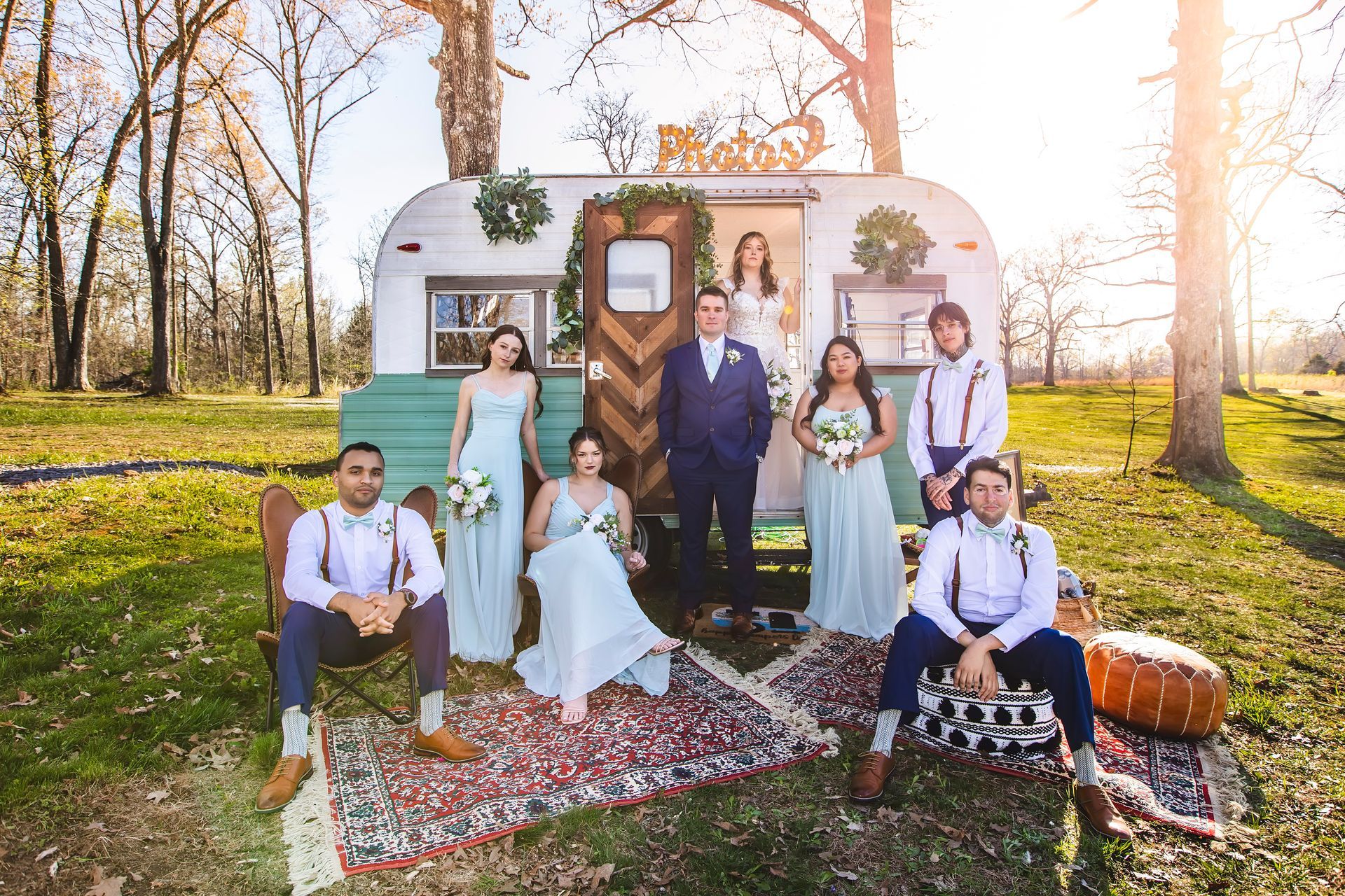Group posing in front of a white vintage camper in a sunny autumn field, surrounded by pumpkins and flowers