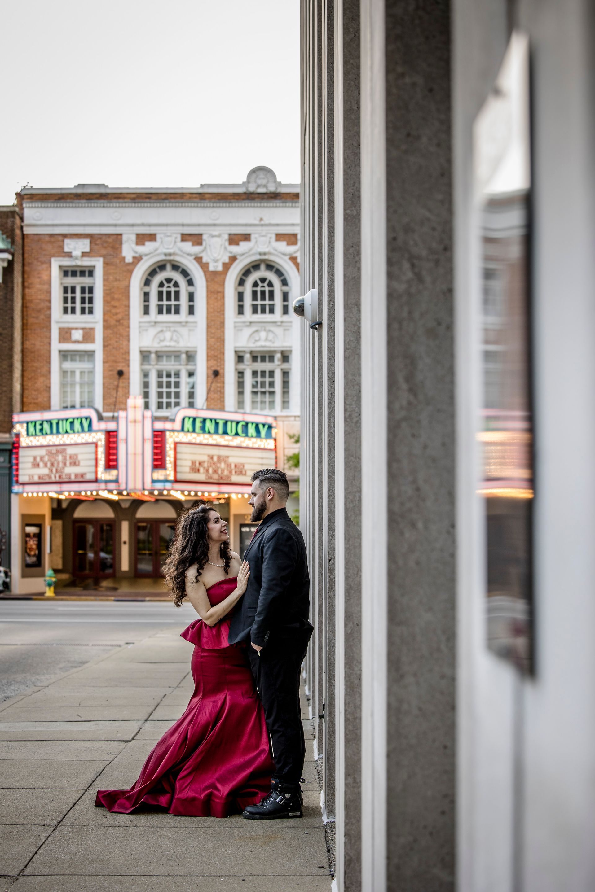 Couple in formal attire posing on a sidewalk in front of a theater building