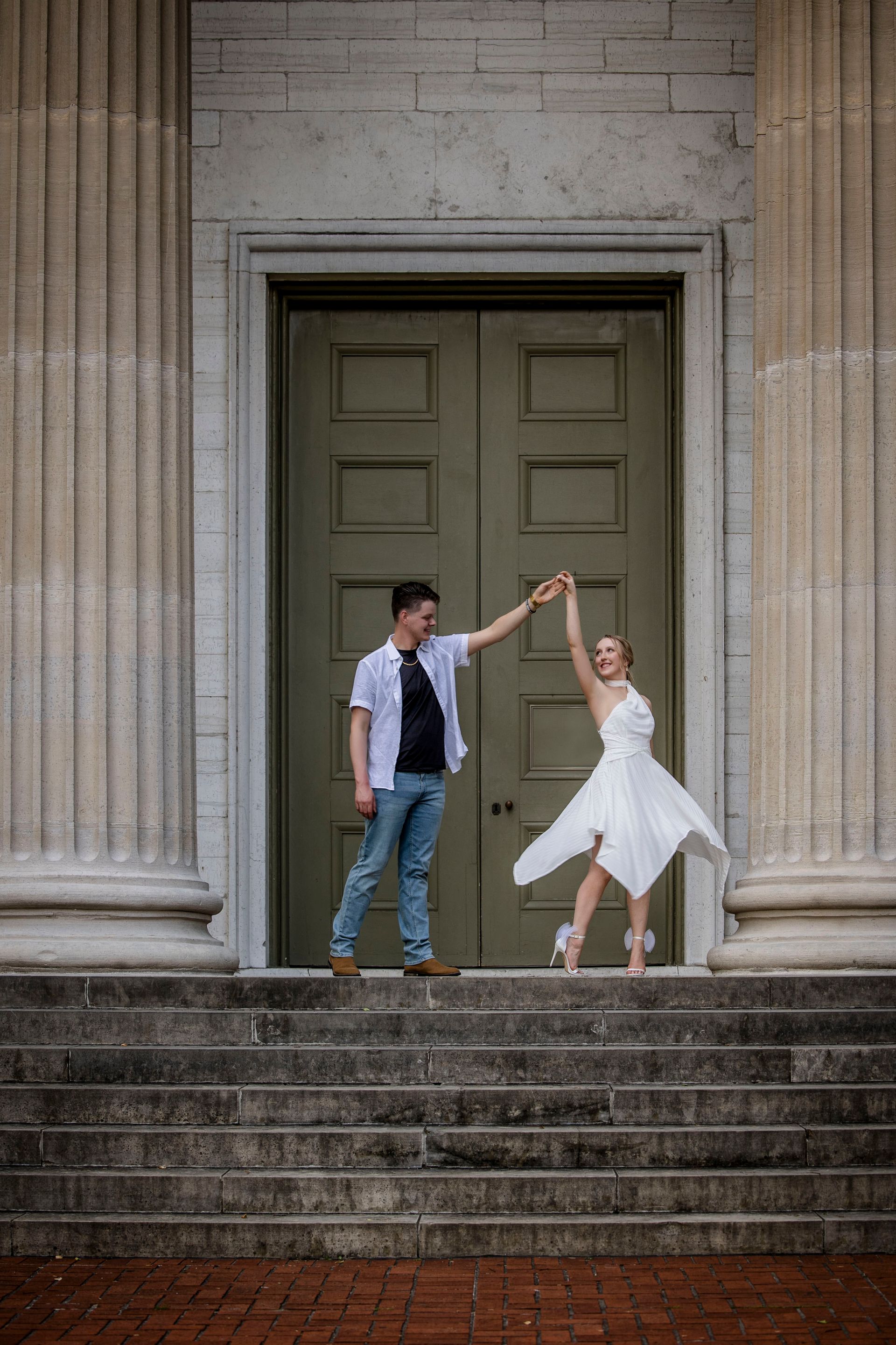 Couple holding hands and dancing on stone steps before a grand doorway