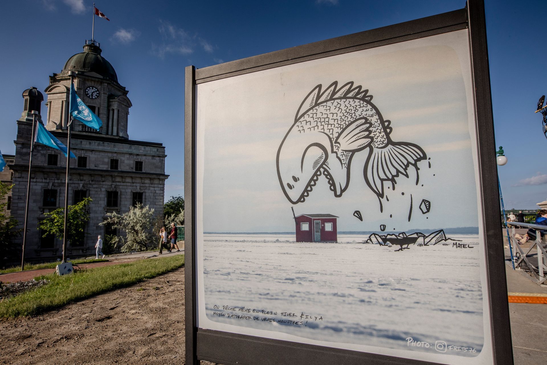 Snow-covered street art panel with a horse-like drawing in front of a historic building under a blue sky