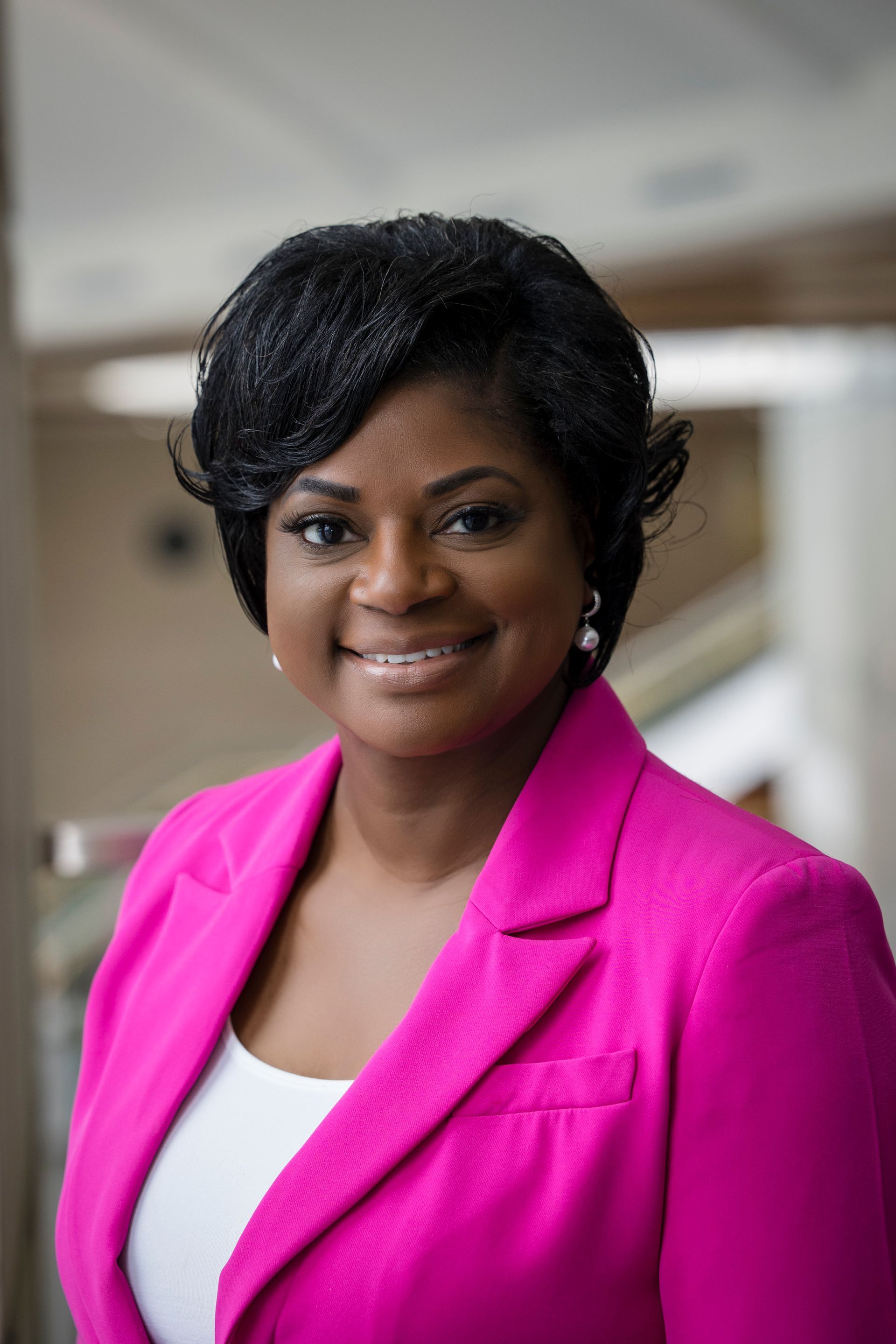 Portrait of a smiling person in a bright pink blazer against a blurred indoor background