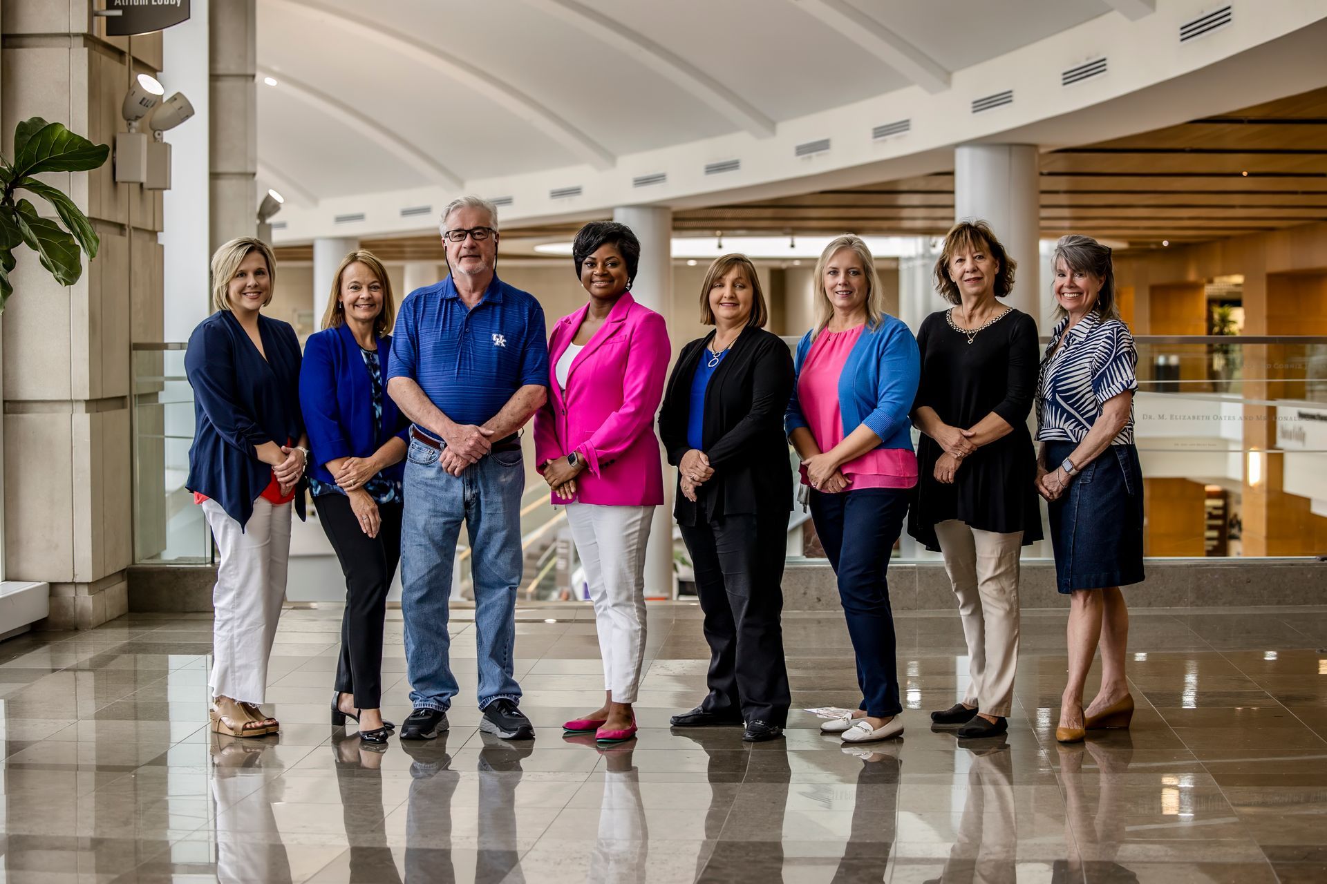 Group of nine people standing together in a bright lobby, posing for a photo.