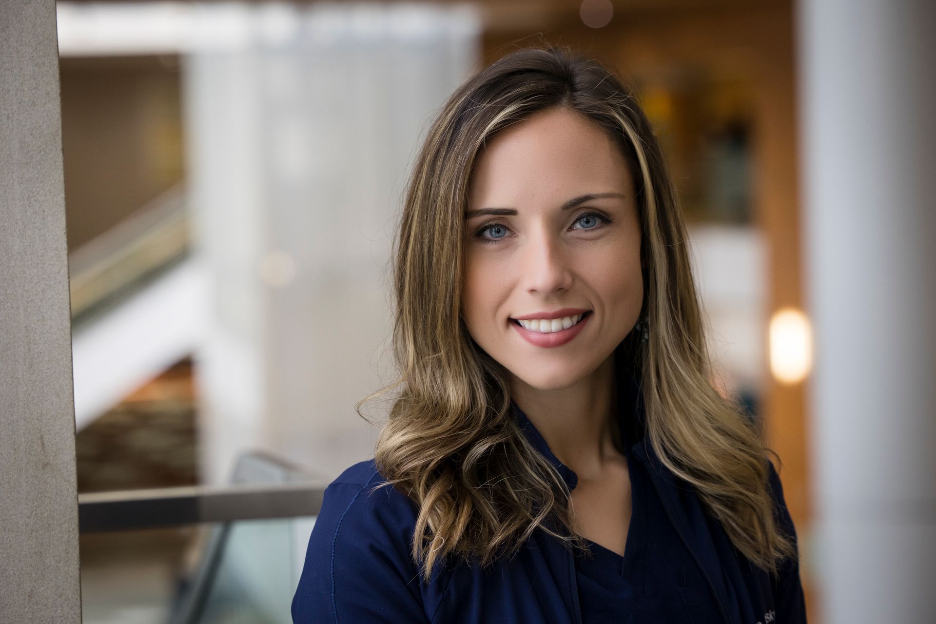 Portrait of a smiling woman in a navy blouse indoors, with a softly blurred hallway background