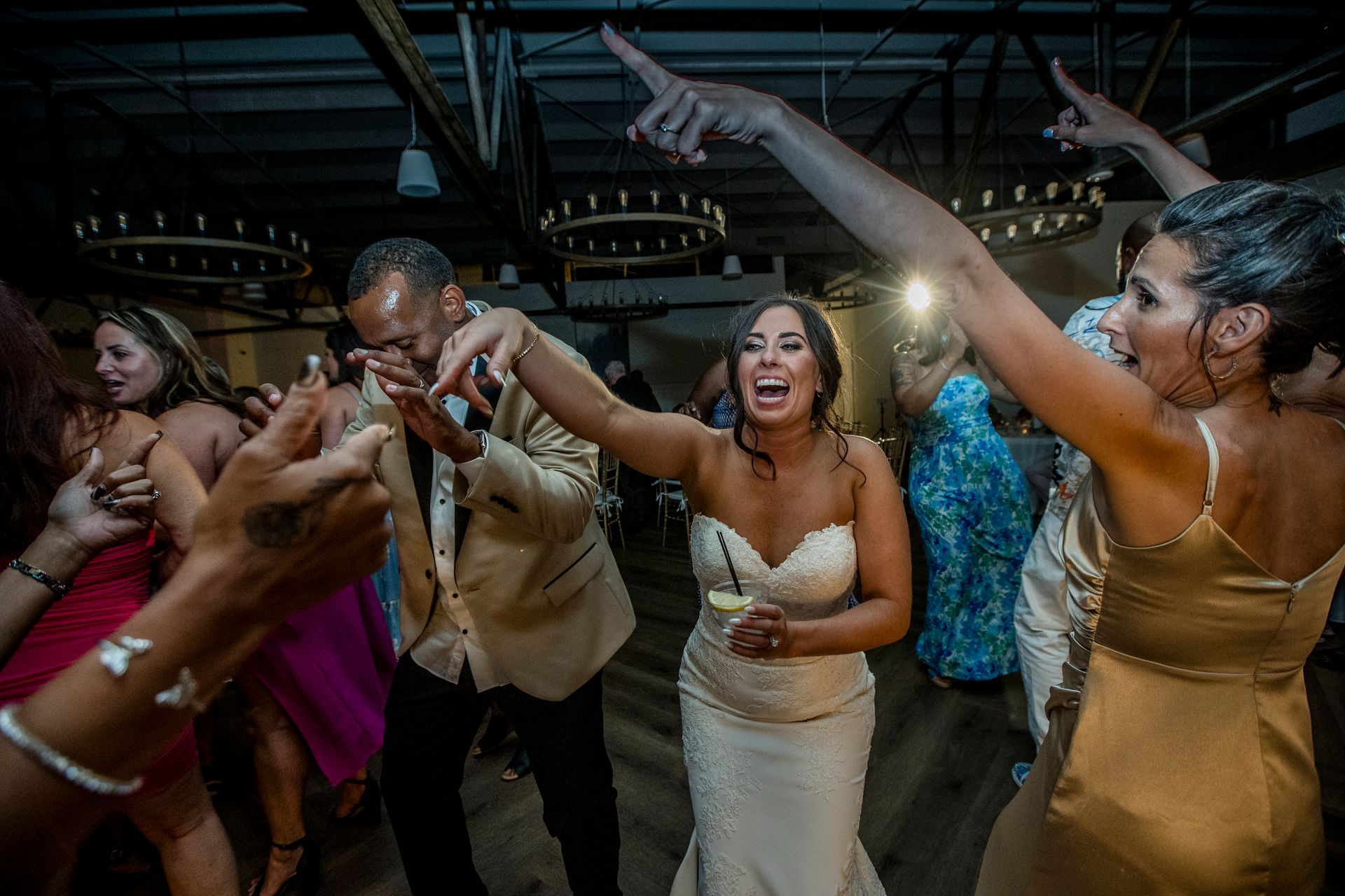 People dancing and cheering at a lively indoor party, with drinks raised and bright lights overhead