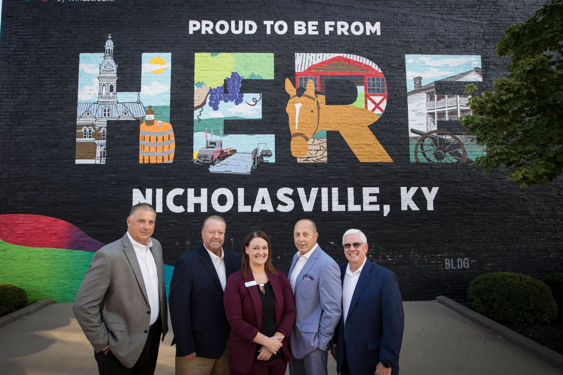 Four people stand before a mural reading “Proud to be from Nicholasville, KY.”