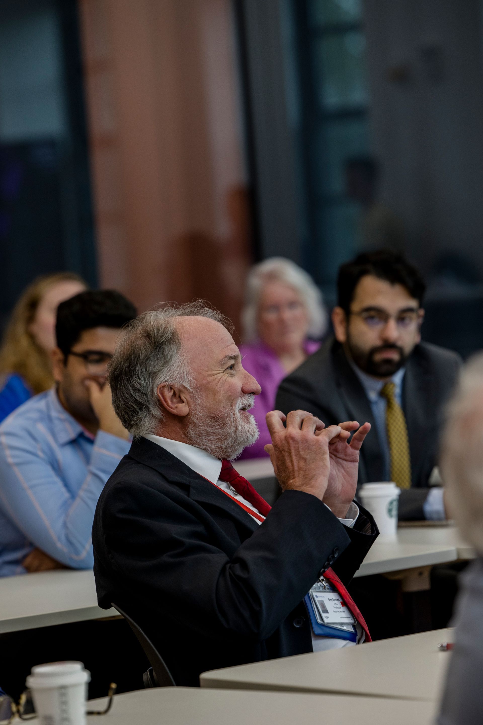 Audience members seated at a table, listening attentively in a meeting room