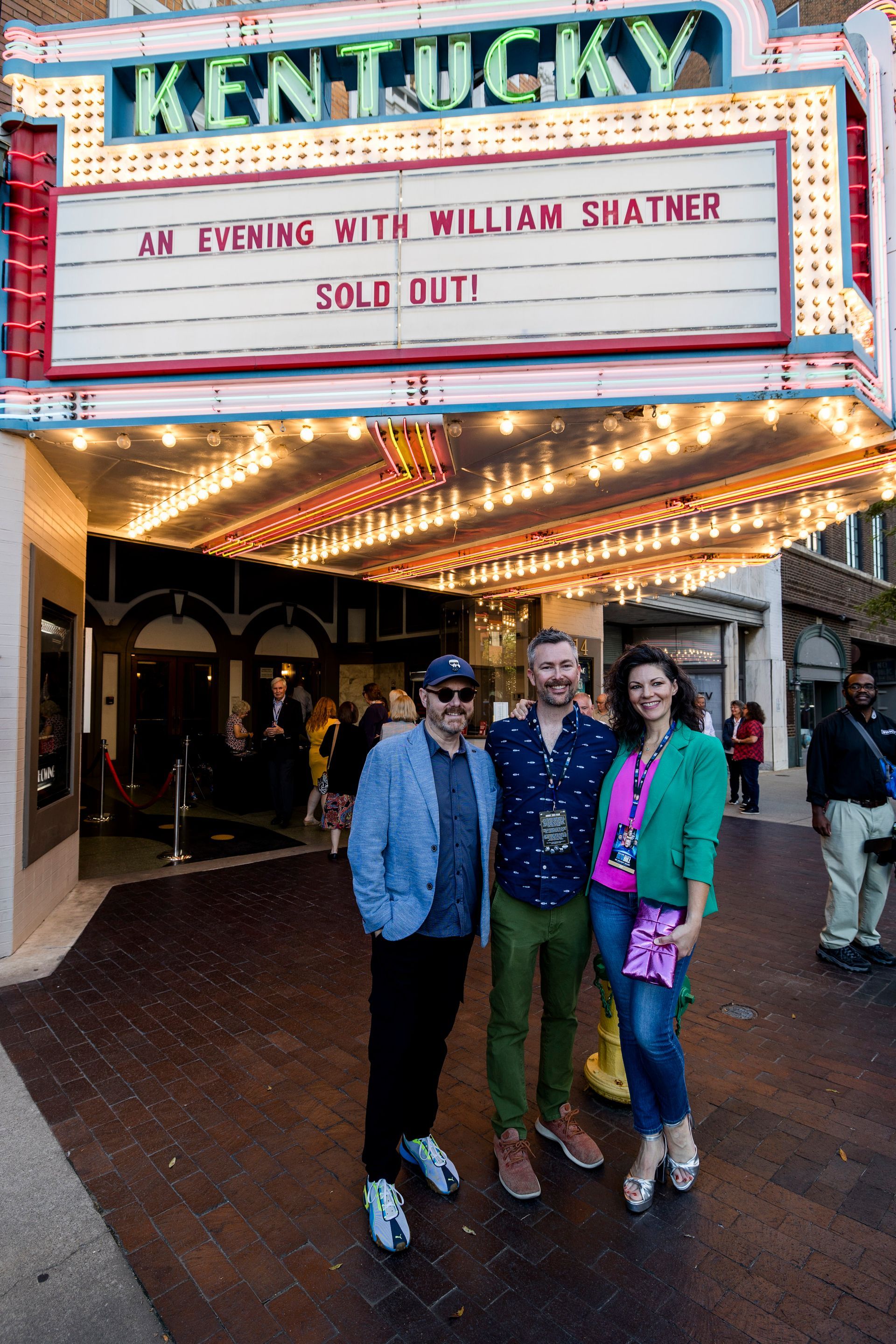 Three people pose under the Kentucky theater marquee at night.