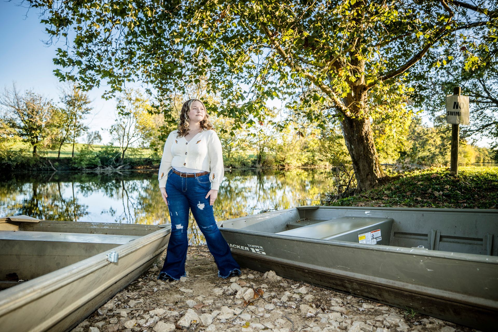 Person standing between two boats by a lakeside under trees