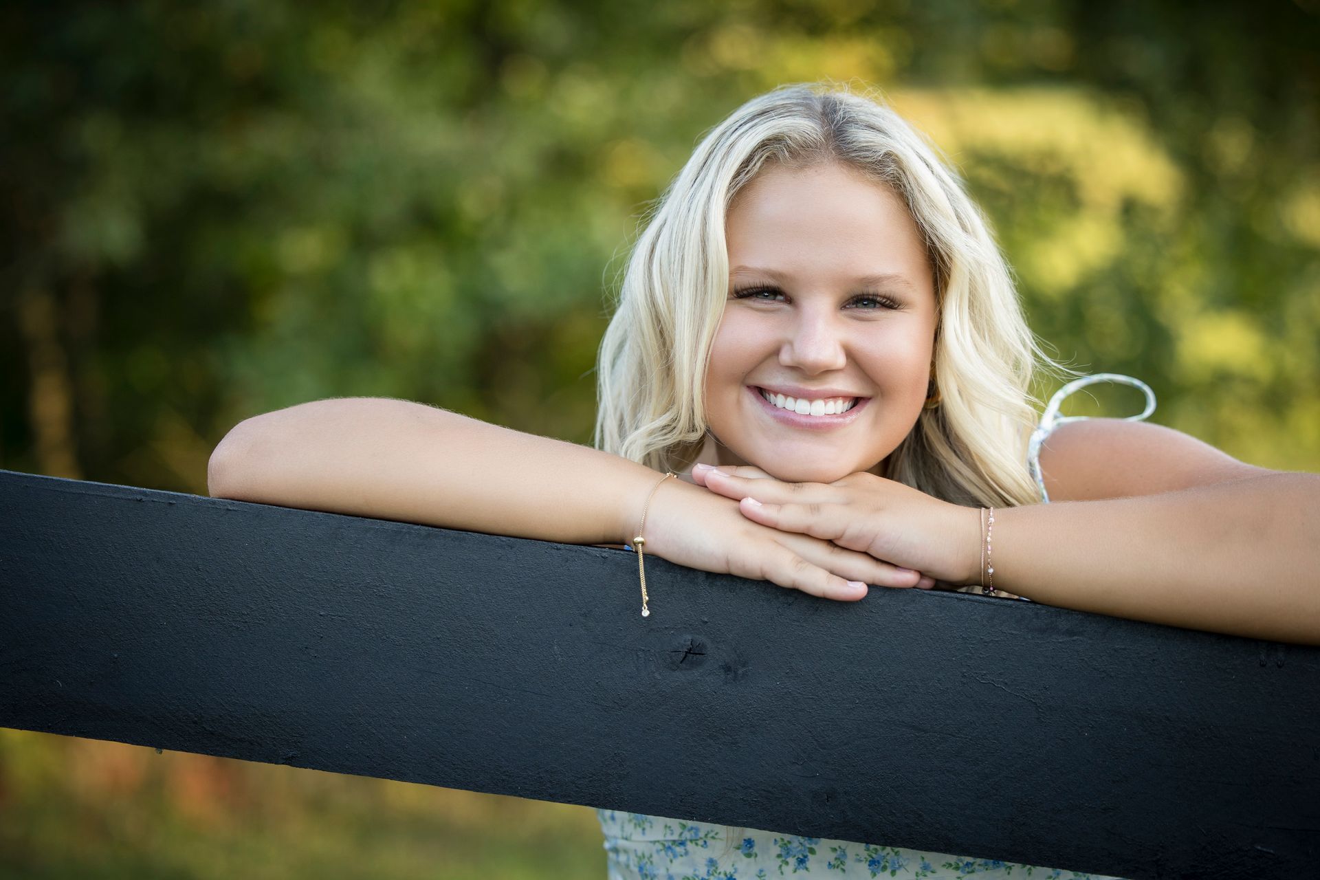 Smiling woman leaning on a black fence outdoors with blurred green background