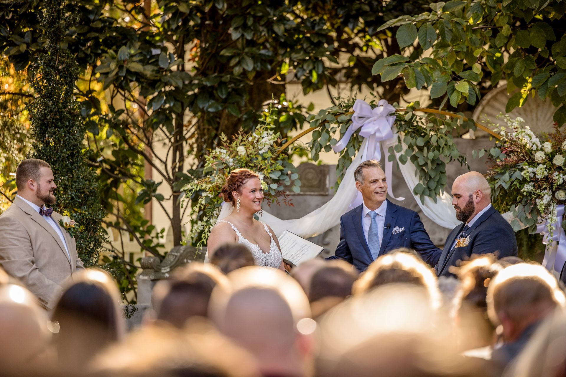 Bride and groom at outdoor wedding ceremony with officiant and guests in foreground