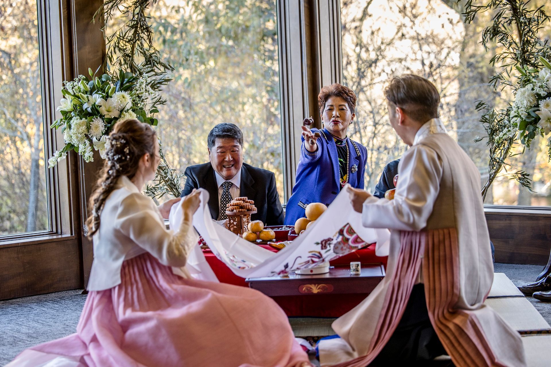 Four people sharing drinks at a table by large windows, with floral decor and warm daylight