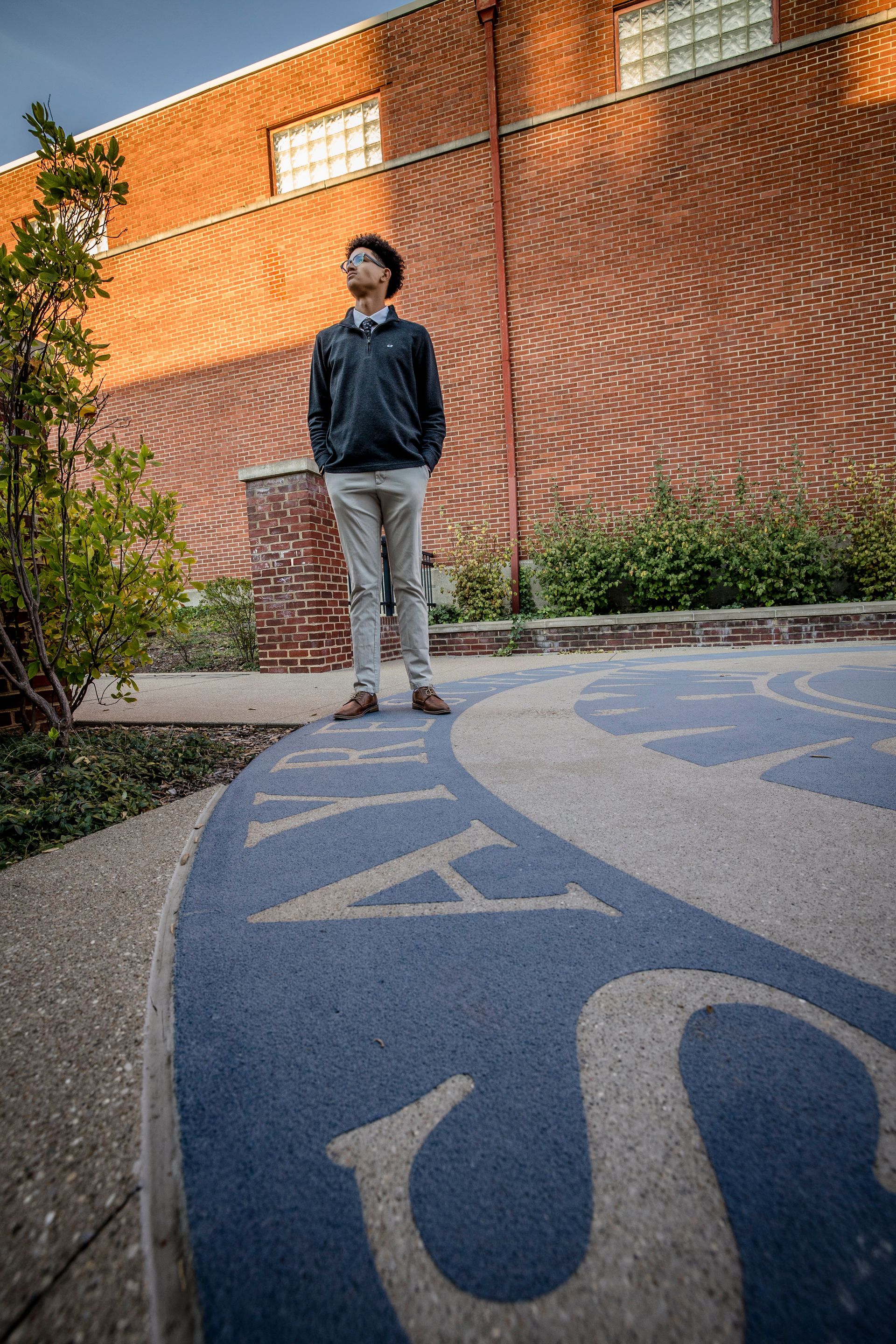 Person standing on a blue pathway beside a brick wall and greenery outdoors.