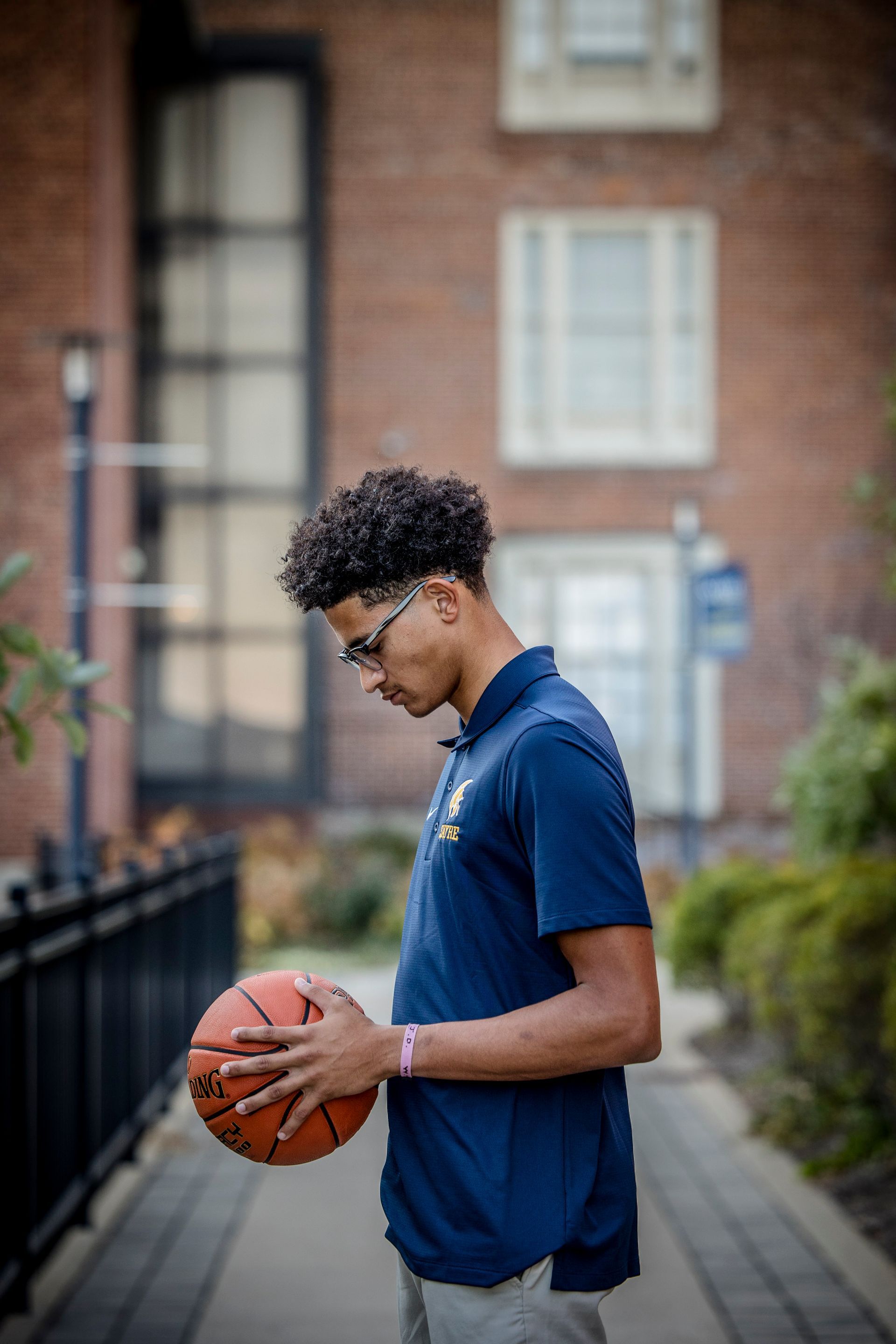 Person in a navy polo holding a basketball on a sidewalk, with apartment buildings in the background
