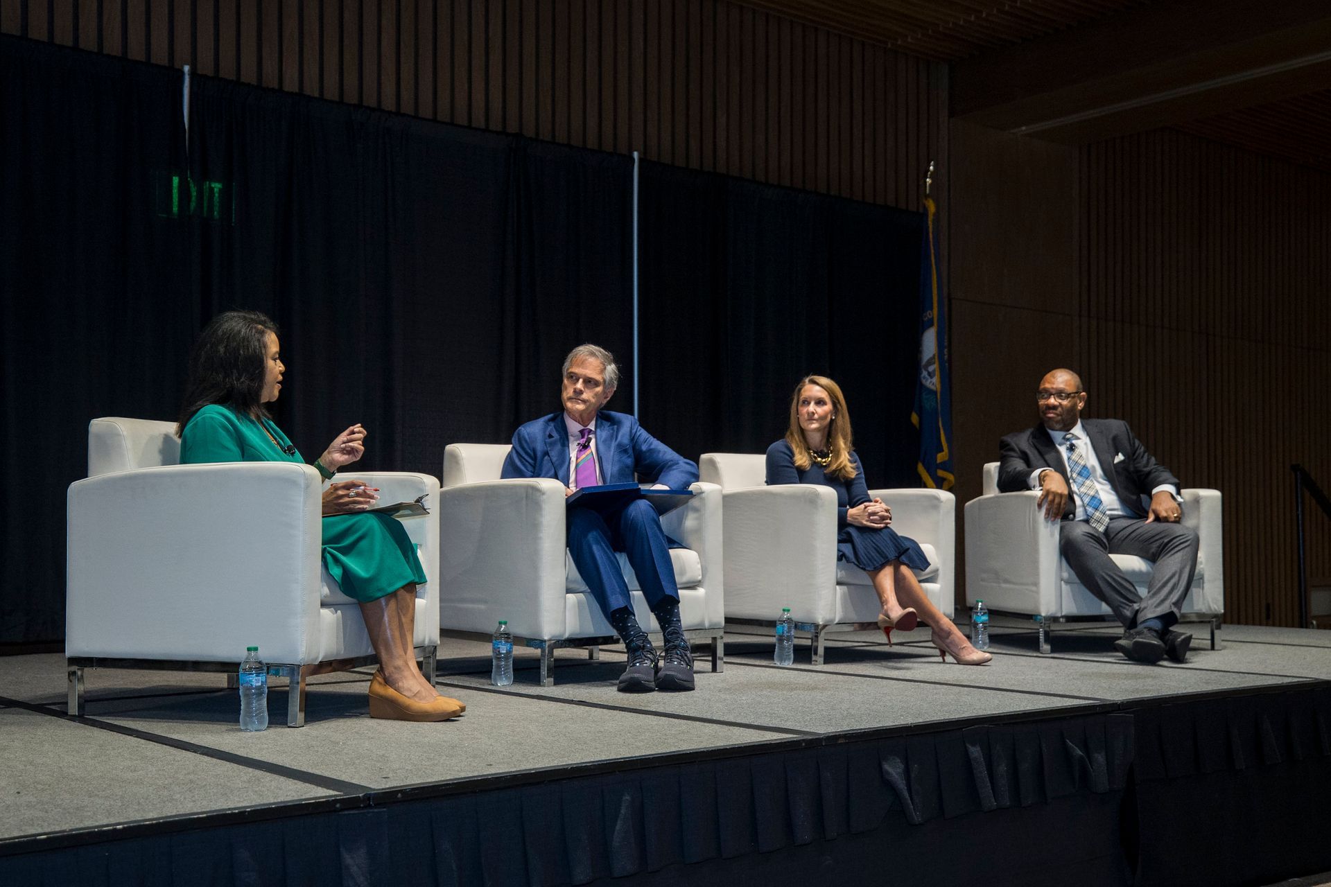 Four speakers seated on stage in armchairs during a panel discussion