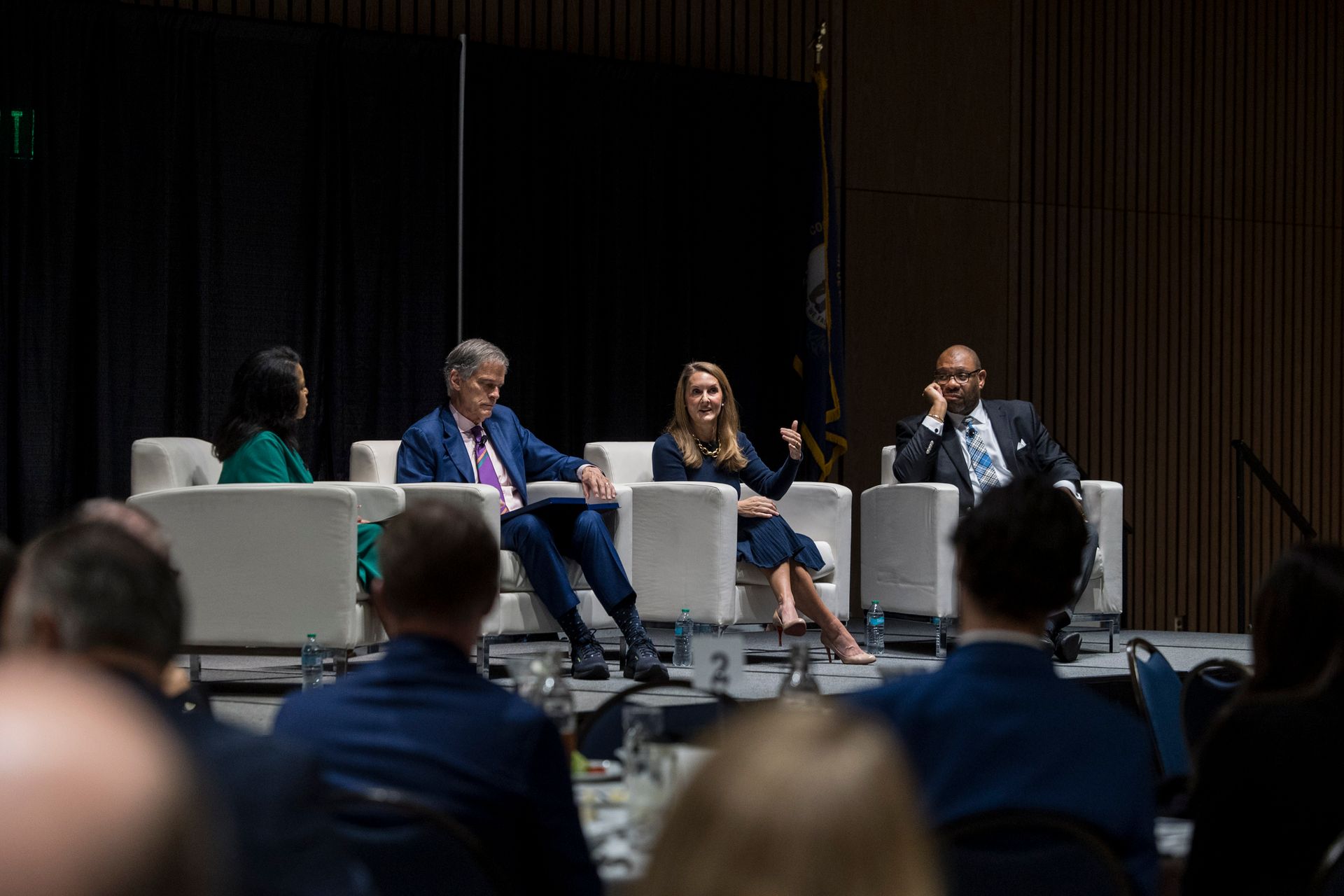 Panel discussion on stage with four speakers seated in white chairs before an audience