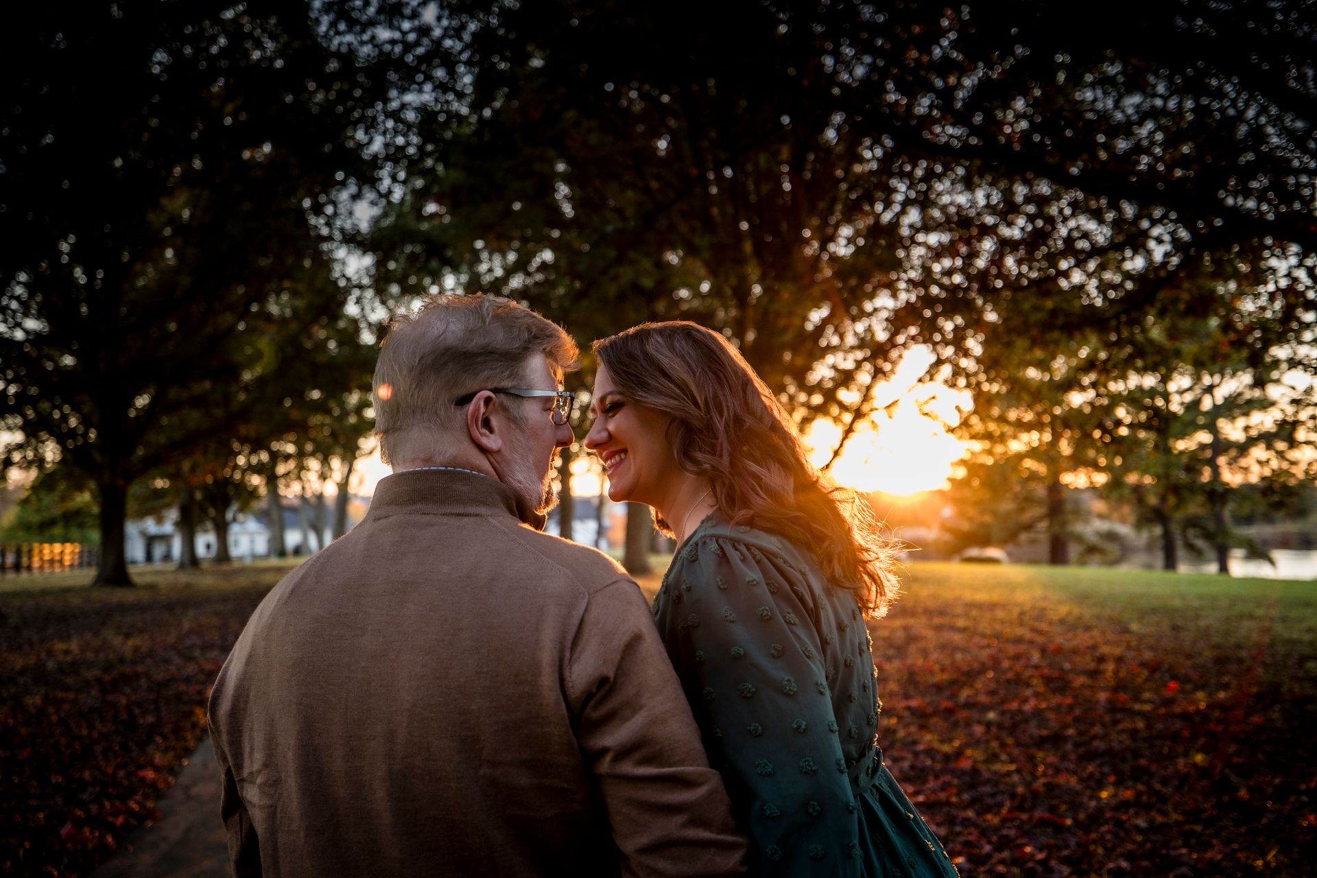 Two people facing each other at sunset in a park, with warm golden light through the trees.