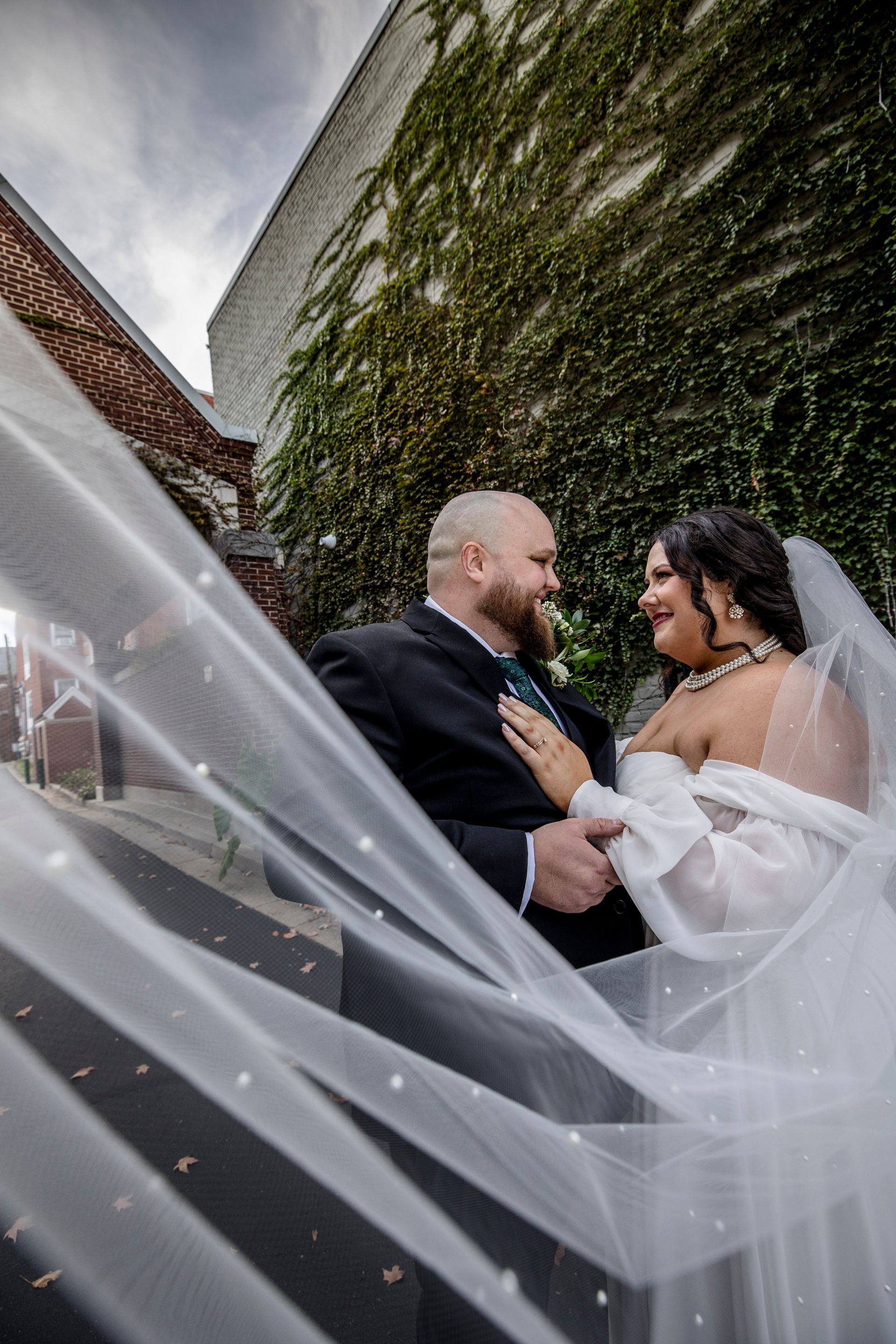 Bride and groom embracing outdoors, with the bride’s veil flowing in the wind