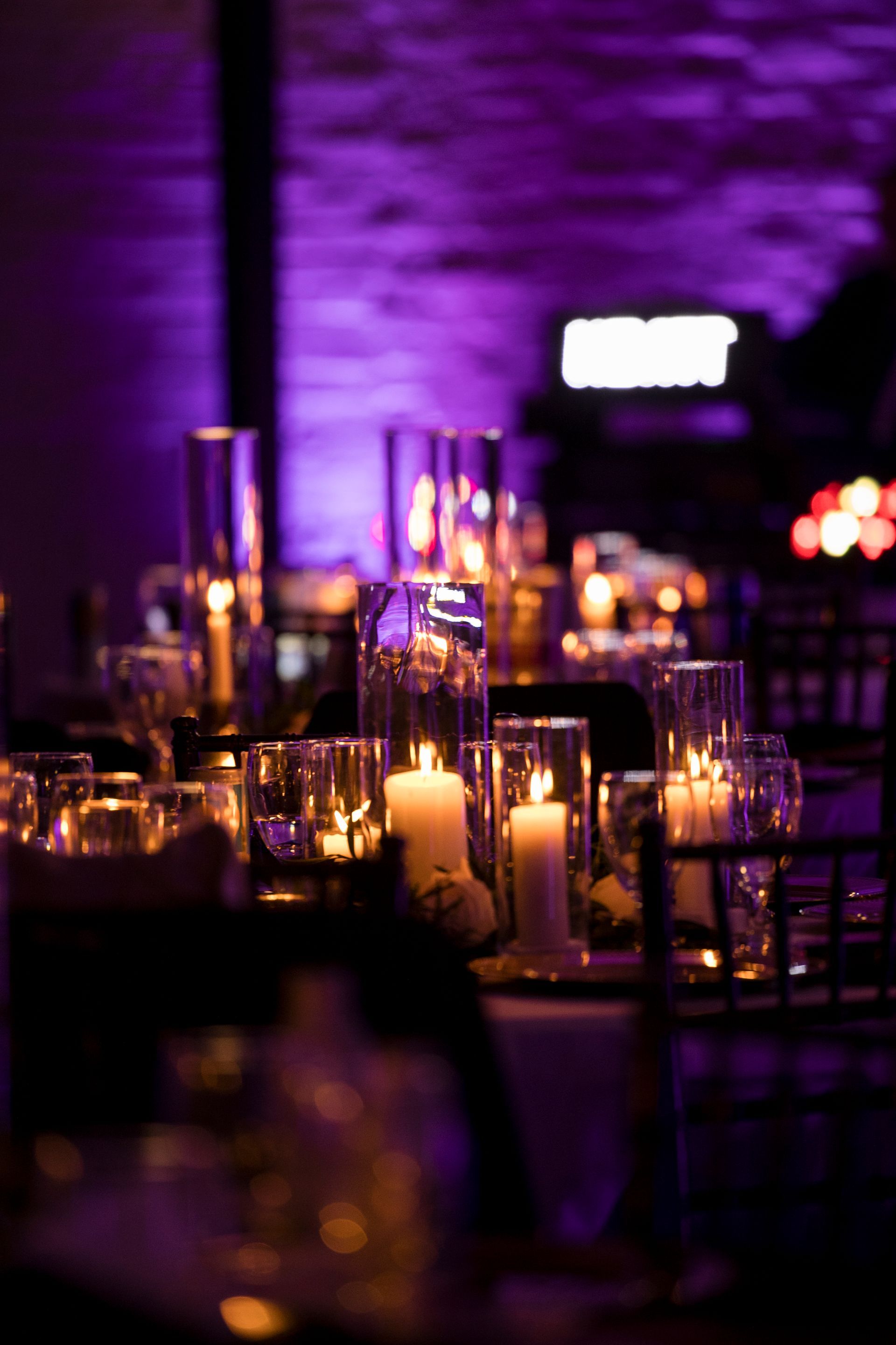 Purple-lit banquet tables with candles and glassware in a dimly lit event space