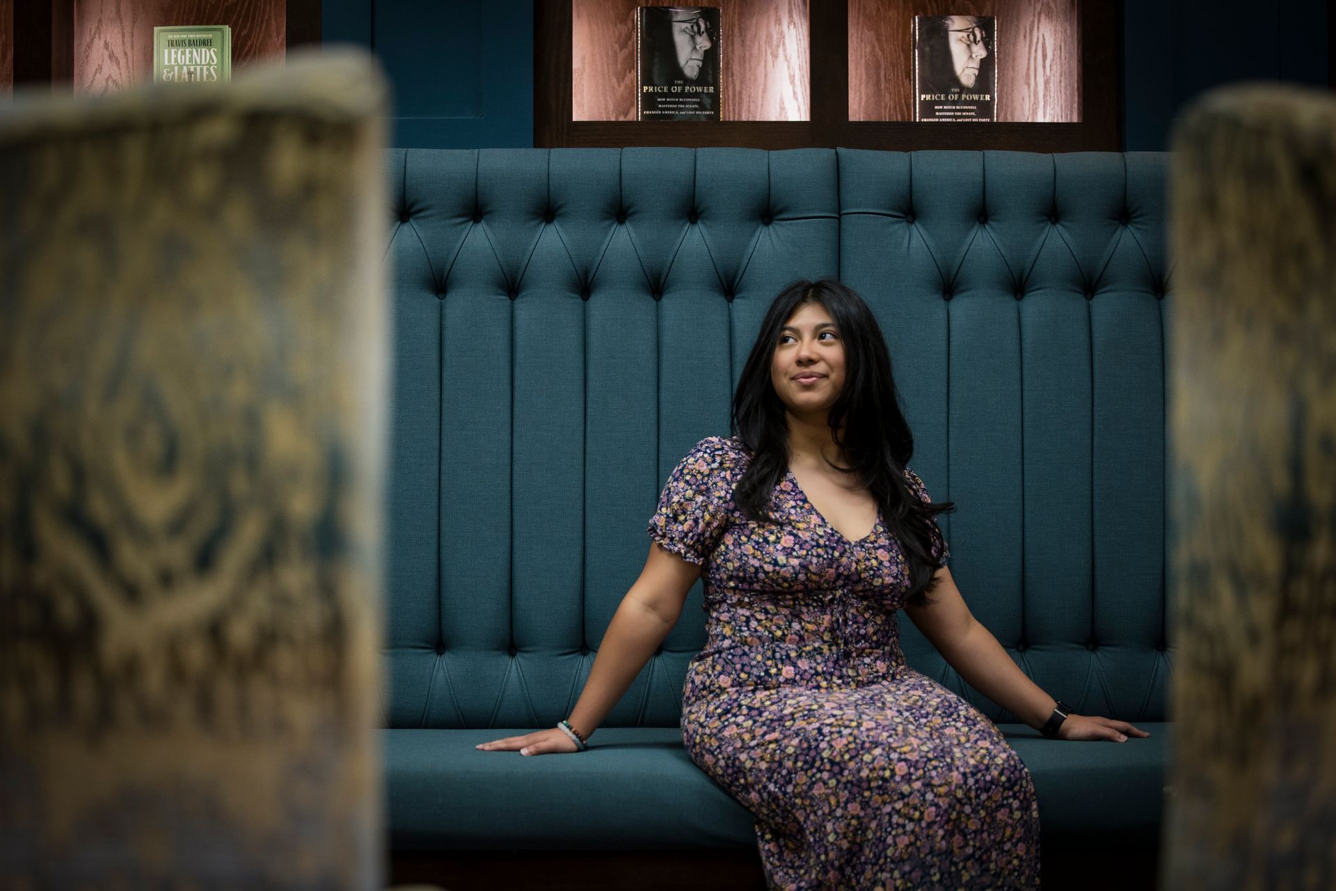 Woman in a patterned dress seated on a teal tufted couch in a dimly lit lounge