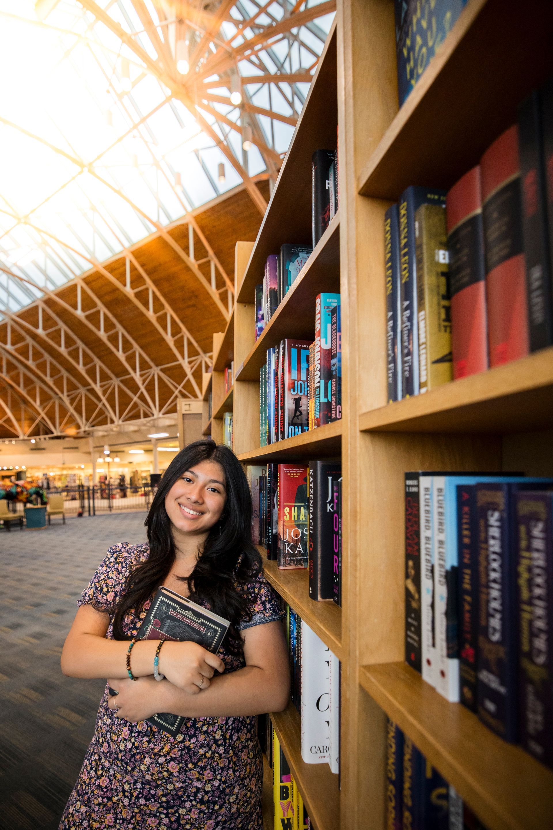 Woman smiling beside a bookshelf in a bright library with a high, sunlit ceiling