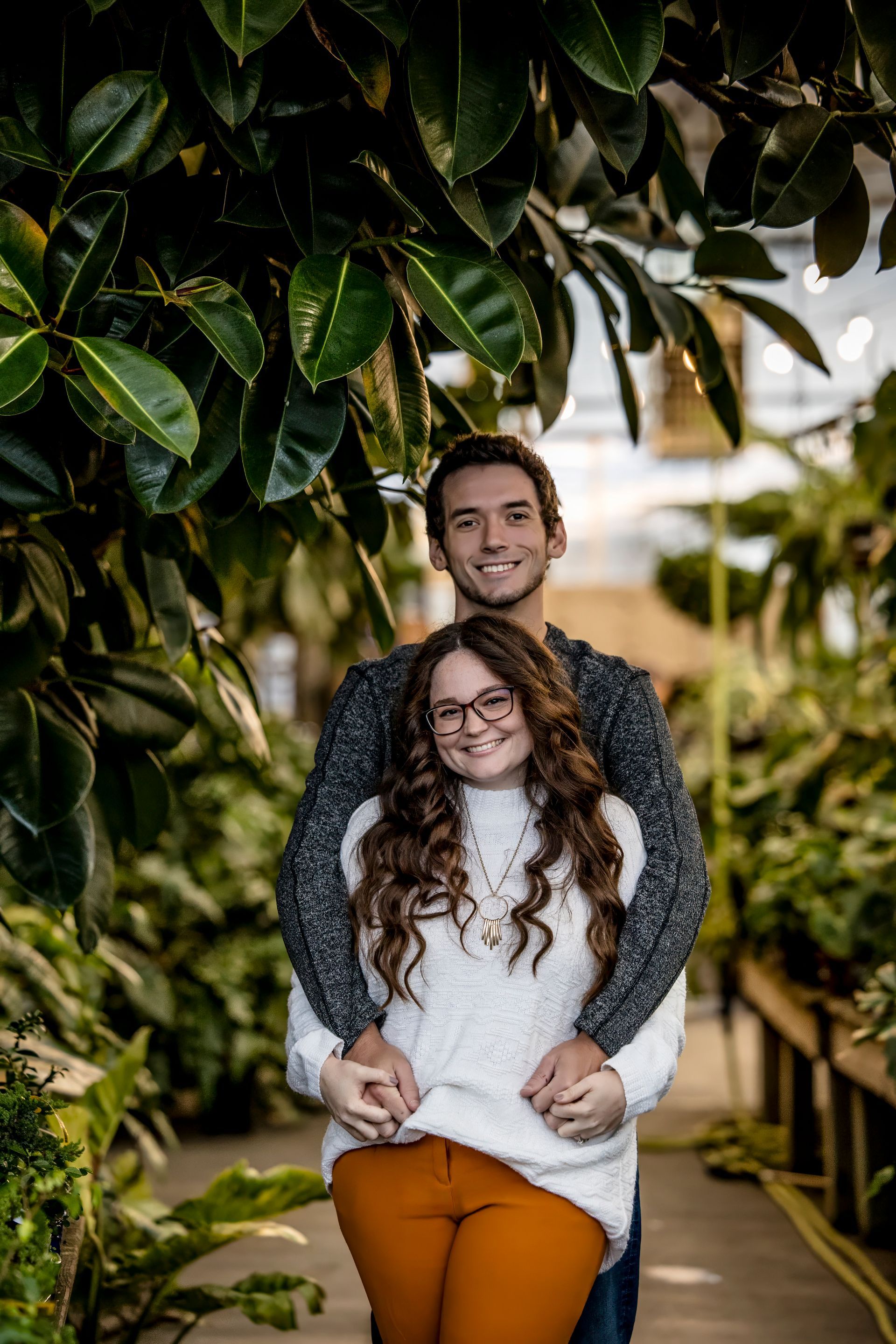 Two people smiling and hugging outdoors on a tree-lined path