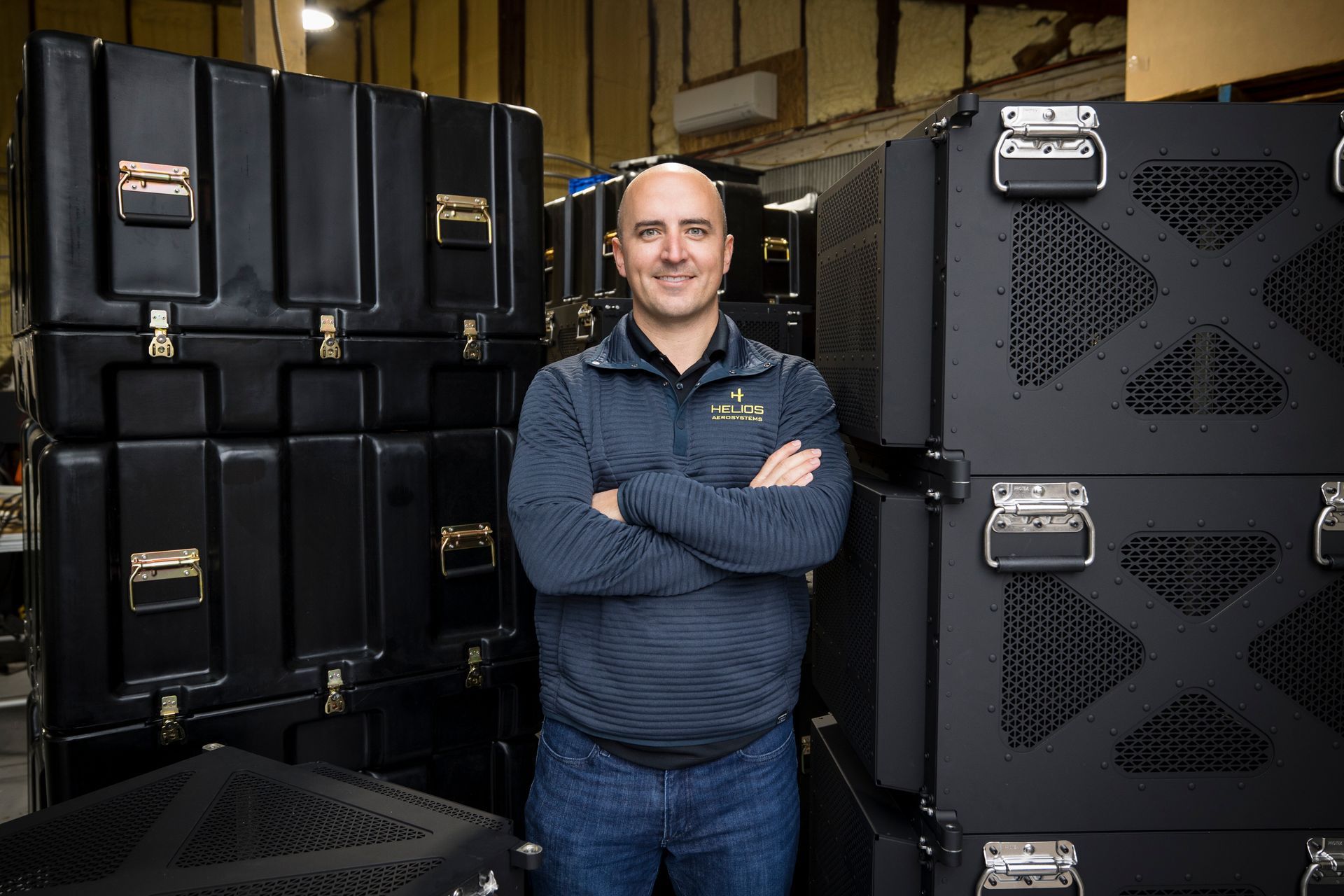 Man standing among stacked black equipment cases in a storage room, arms crossed
