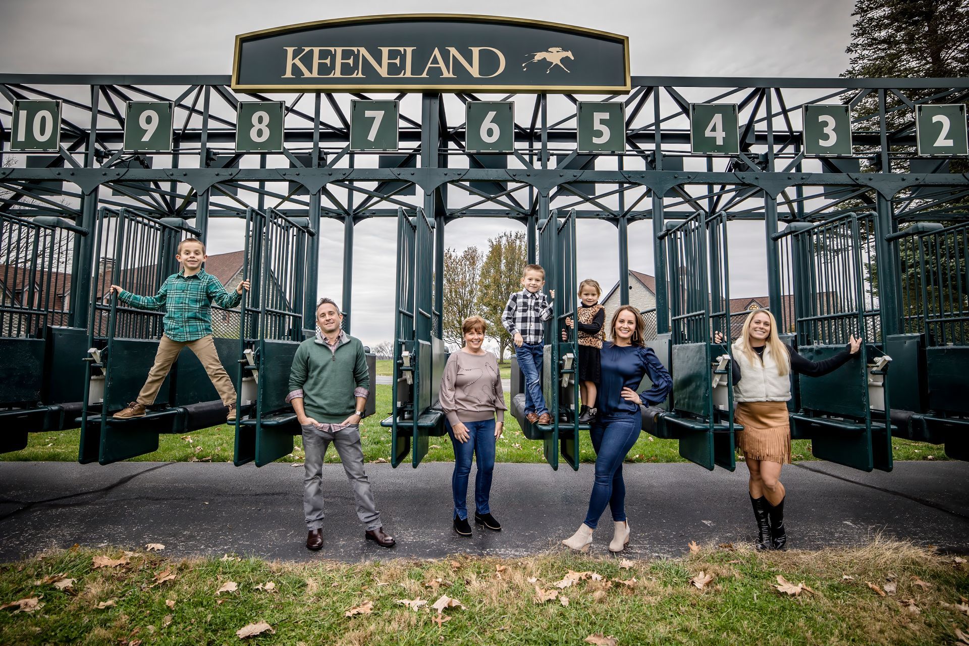 Six people posing on swings in front of a numbered carnival-style sign at Keenan’s