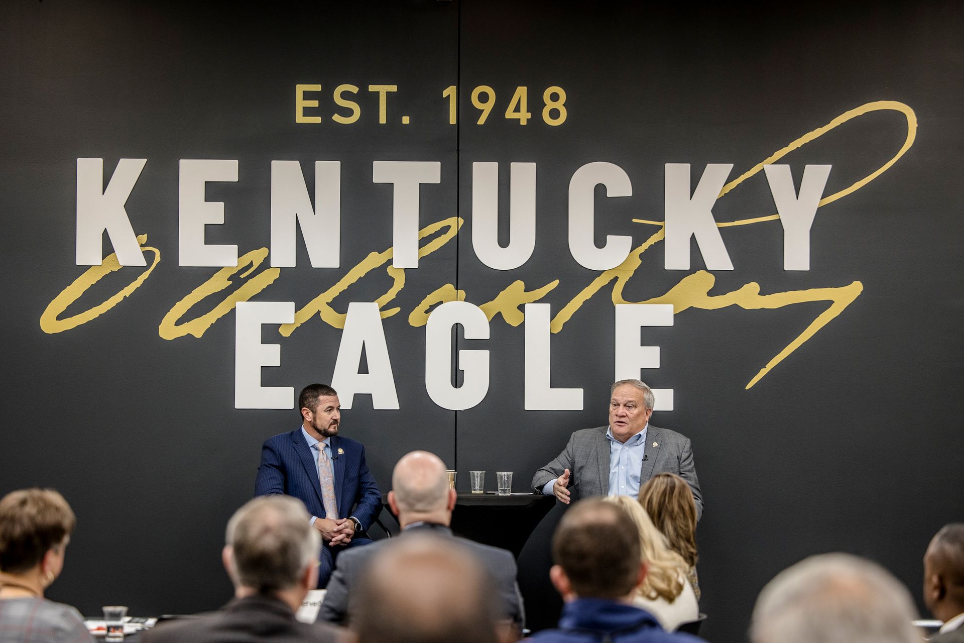 Kentucky Eagle stage event with speakers in front of large “EST. 1948” backdrop