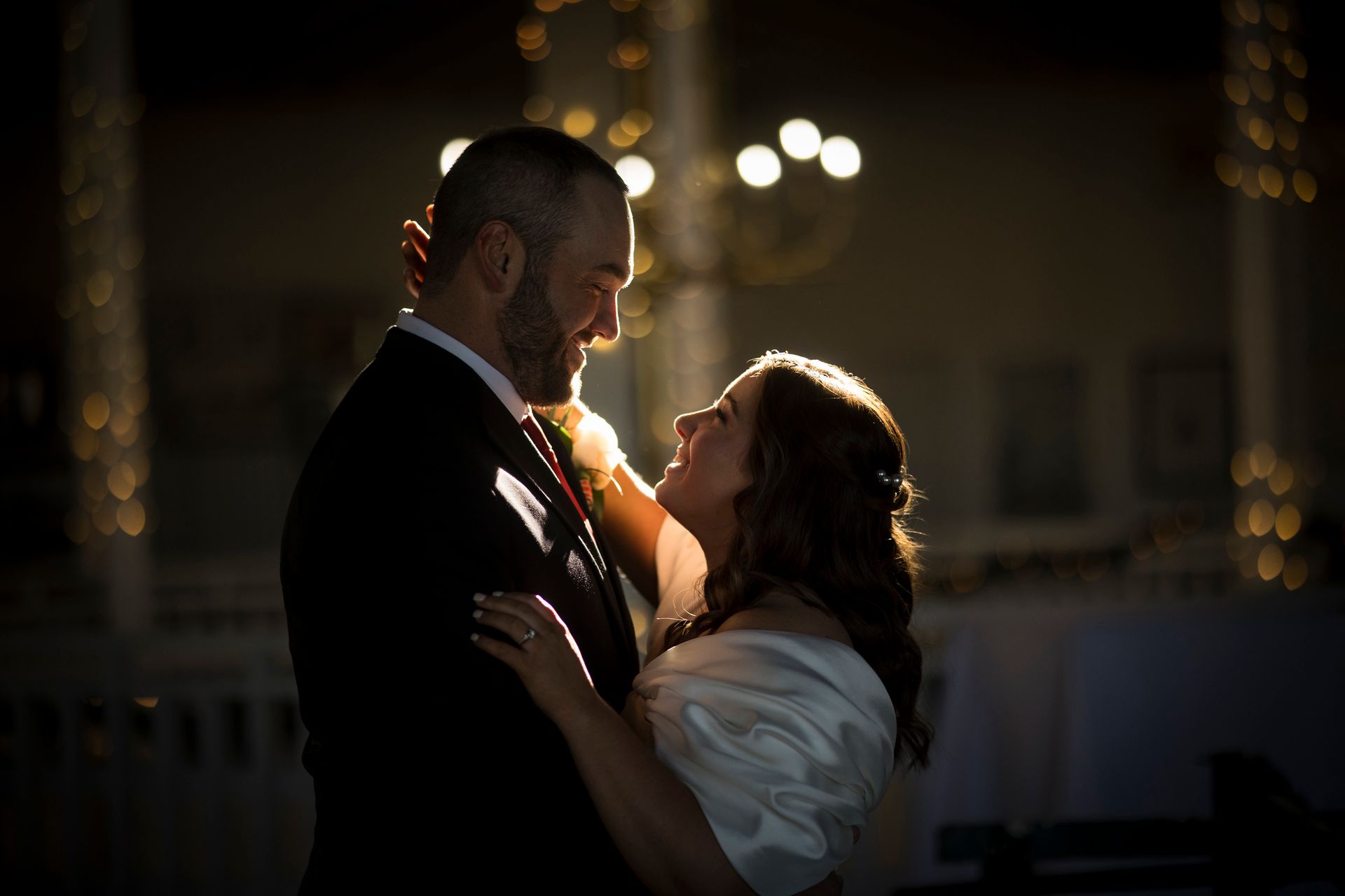 Couple embracing in a dimly lit ballroom, with warm candlelight and blurred lights in the background