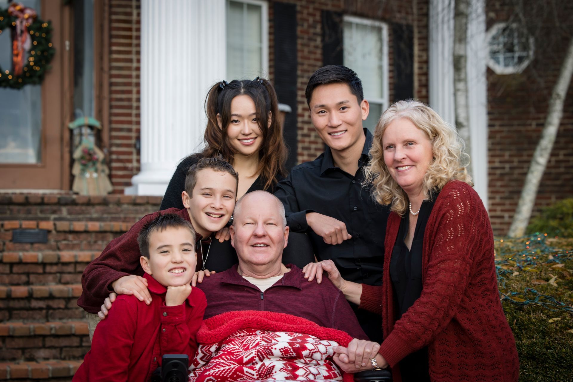 Family gathered on a porch, smiling around an elderly man seated in front.