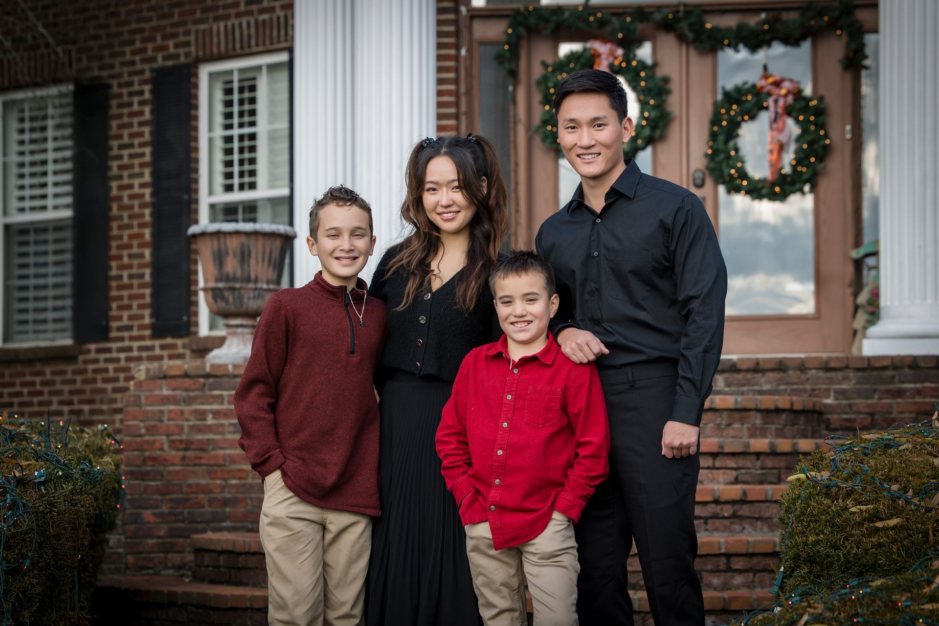 Family of four posing on front porch decorated with holiday wreaths and garlands