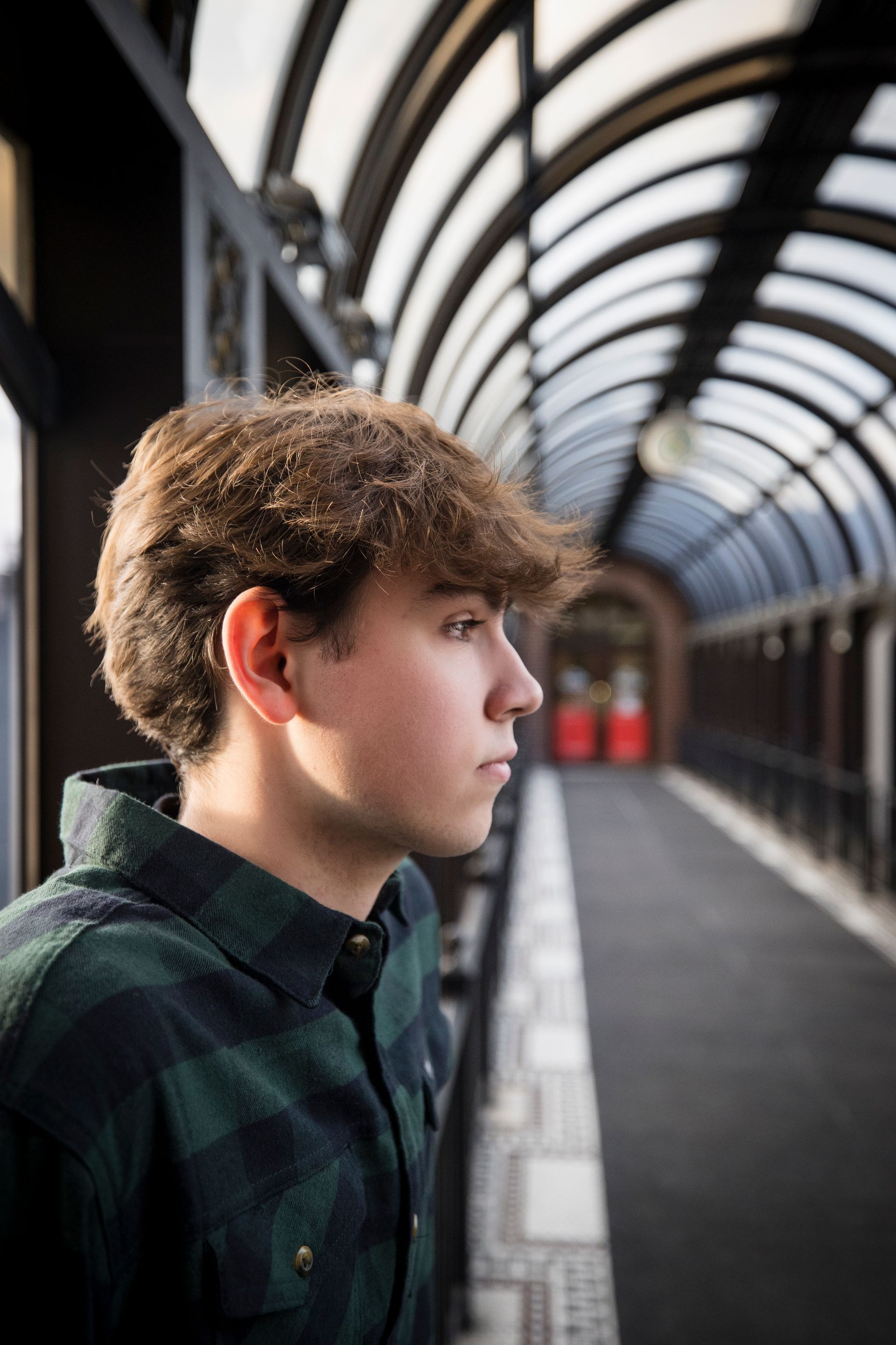 Teen in plaid shirt standing on a covered walkway, looking into the distance.