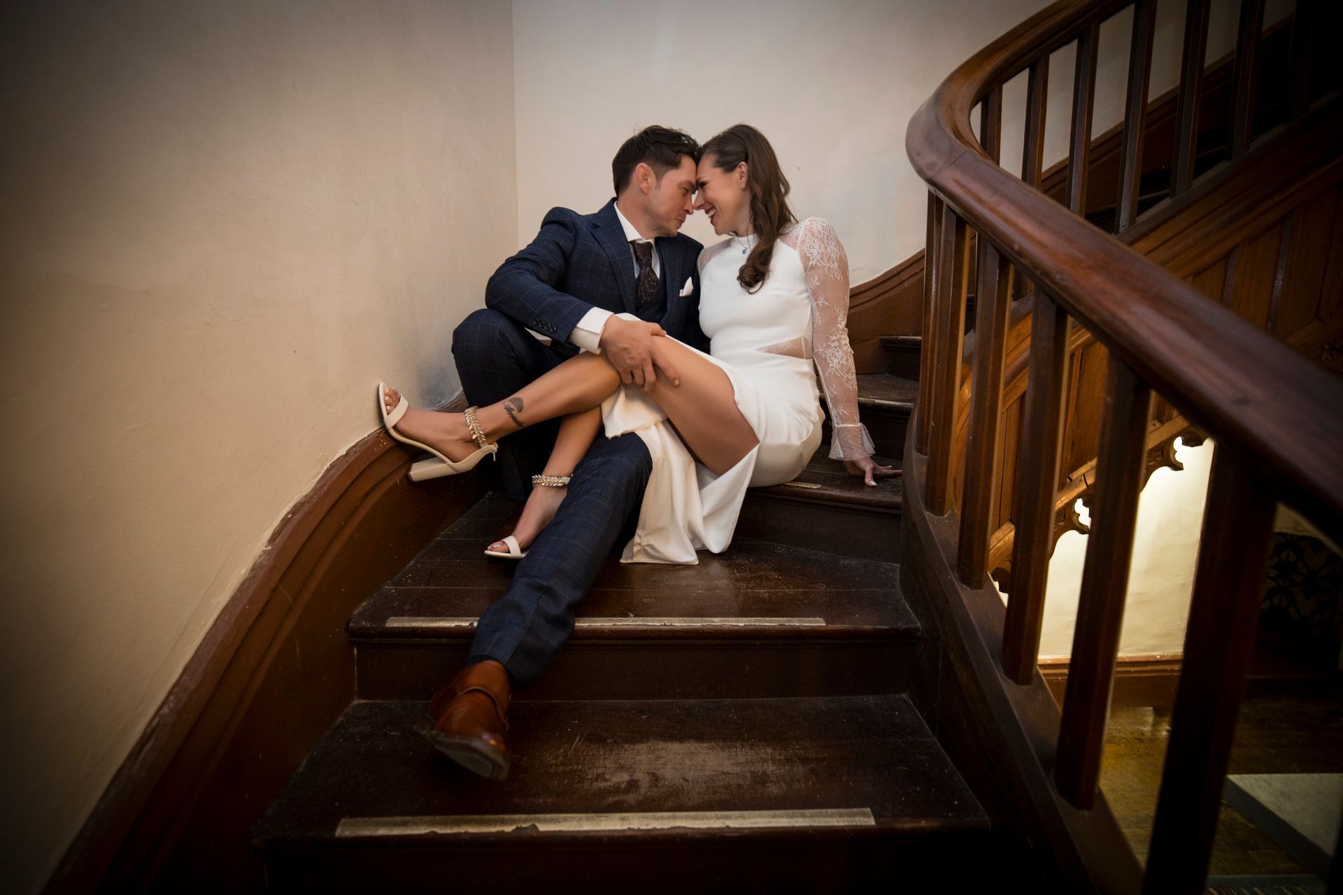 Couple in formal attire kissing on a wooden staircase, with the woman sitting on the steps.