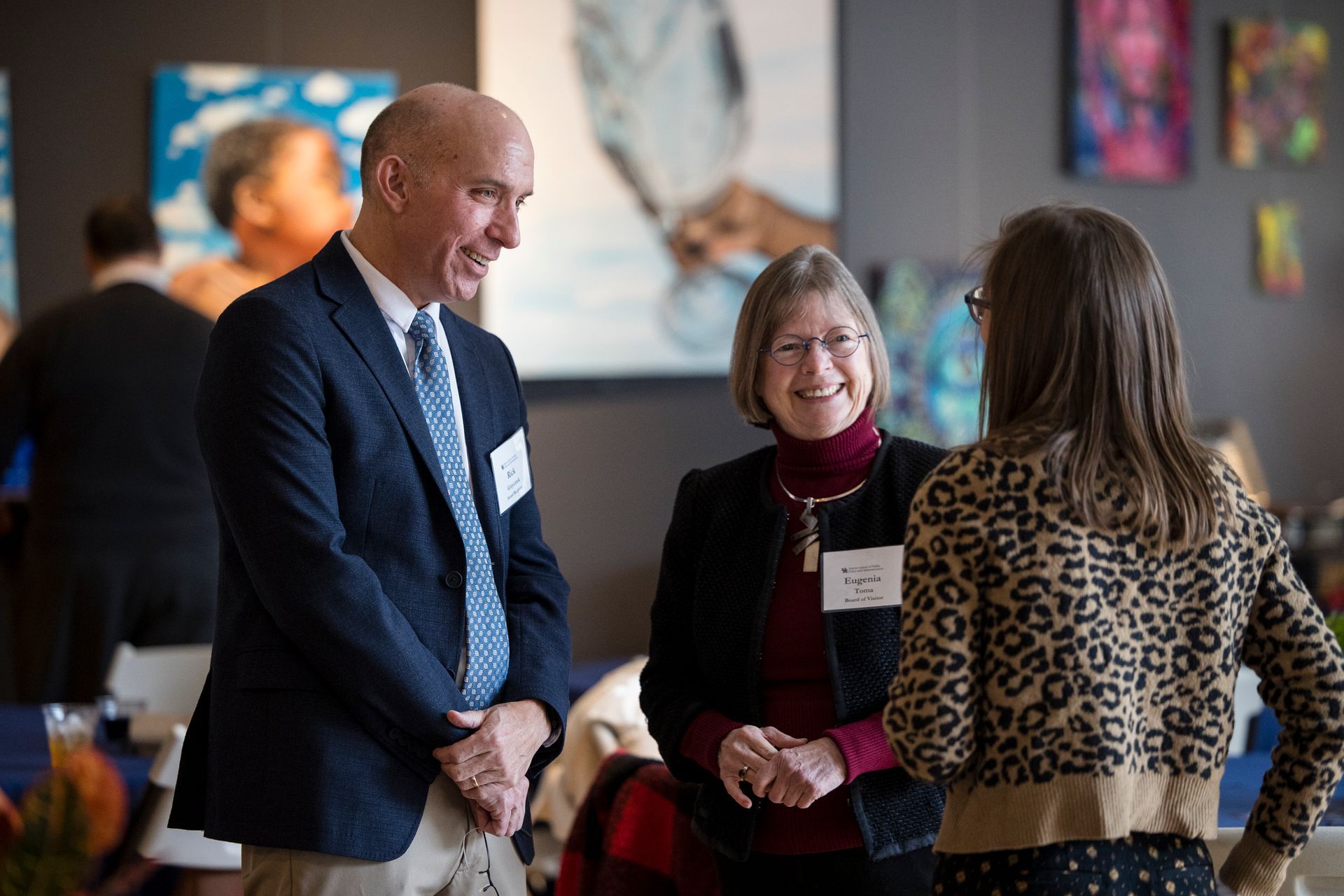 Three people chatting in a gallery, with paintings blurred in the background.