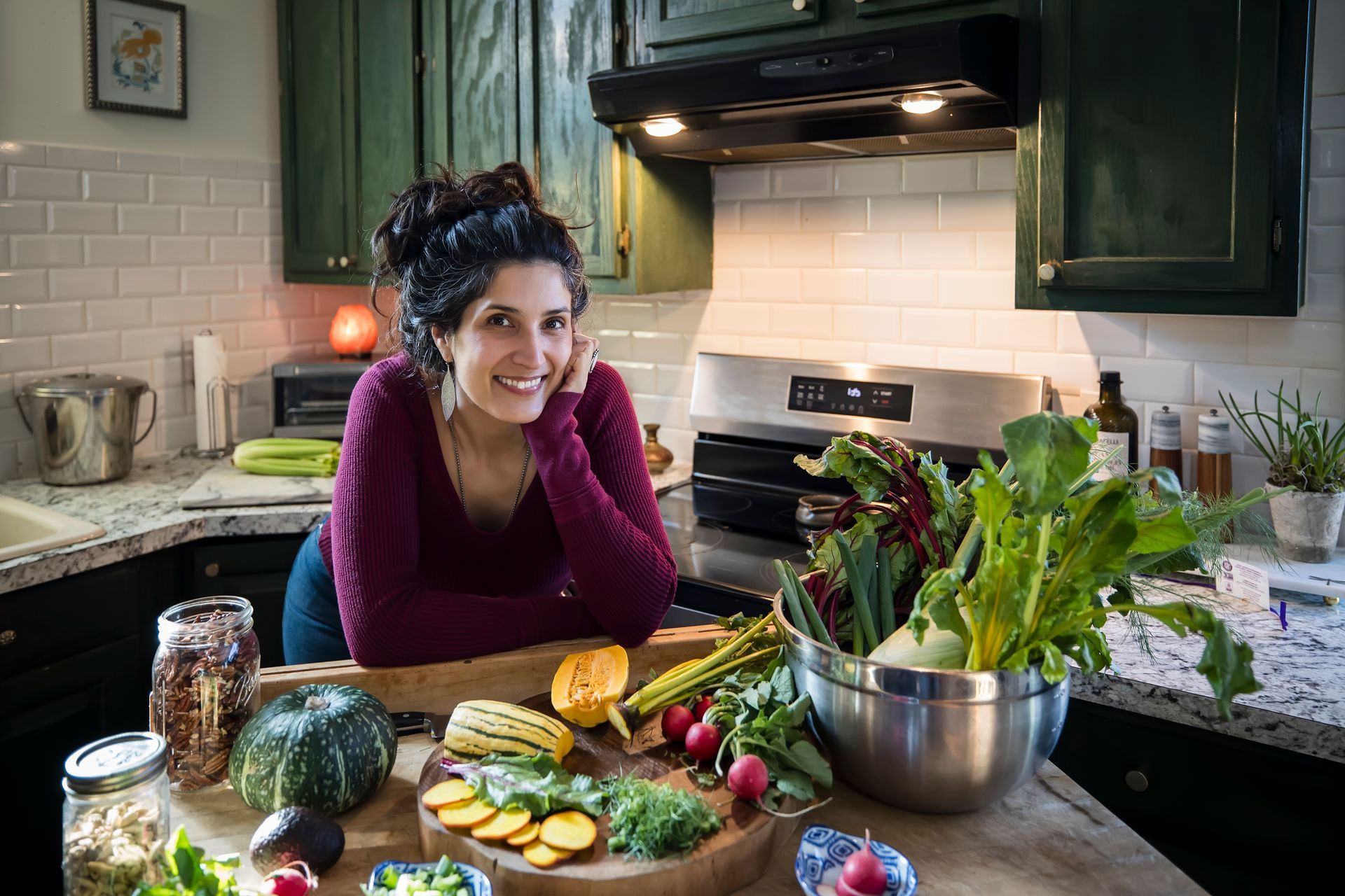 Woman smiling in a kitchen beside fresh vegetables and prepared food on a counter