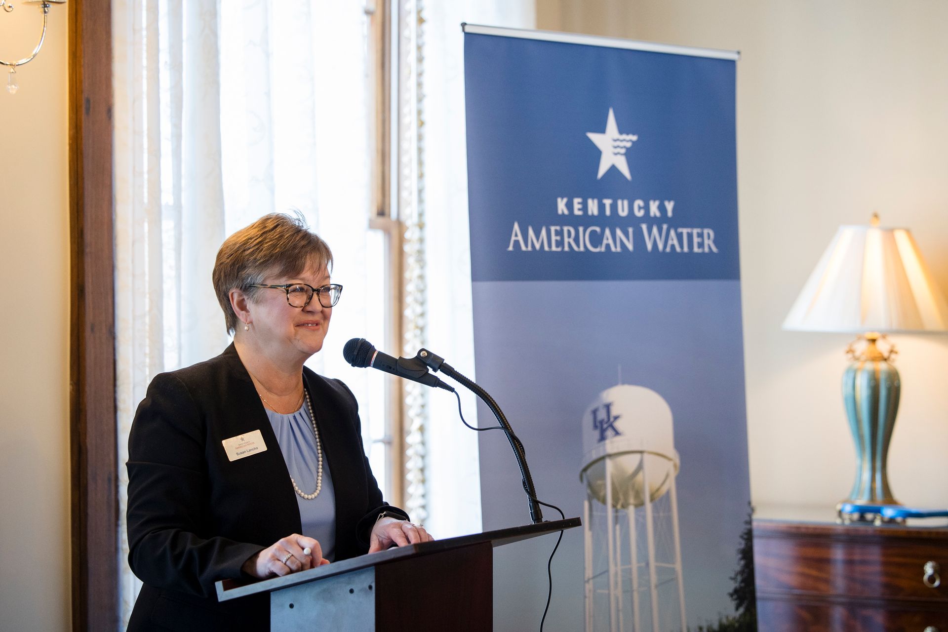 Woman speaking at a podium beside a Kentucky American Water banner in a bright room