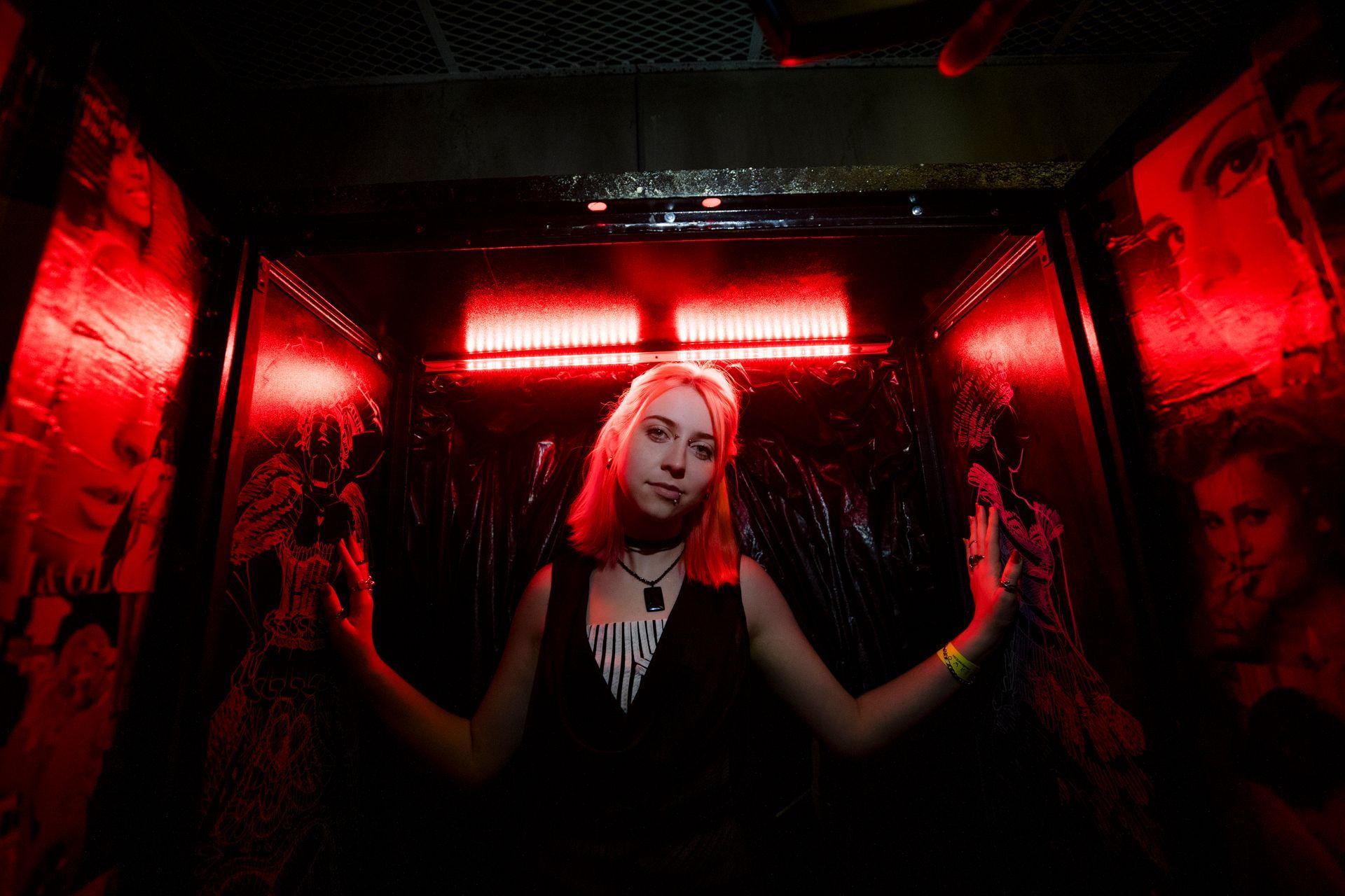 Woman standing in a red-lit nightclub, framed by reflective walls, with hands raised at her sides.