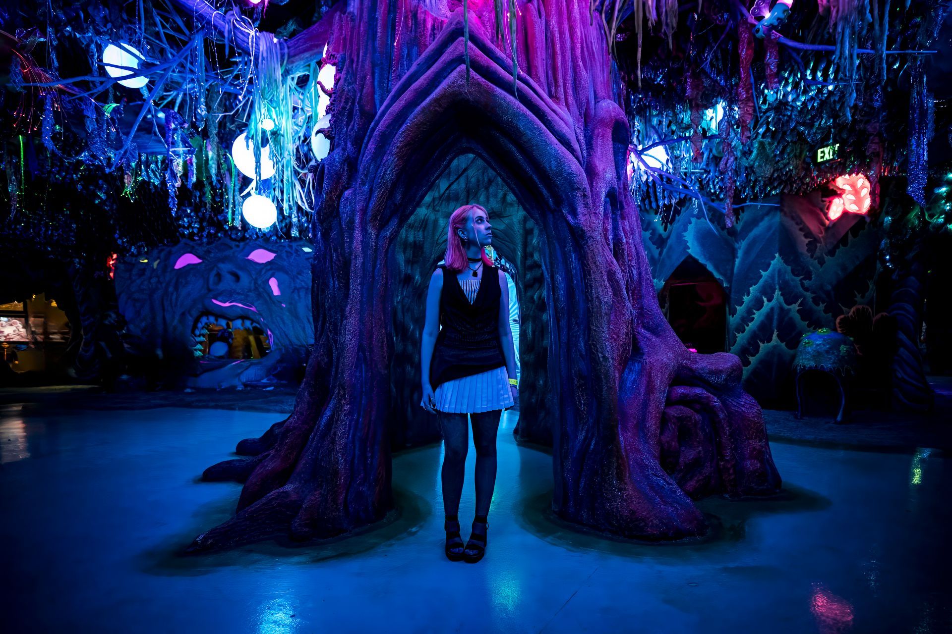 Person standing in a glowing blue-purple fantasy forest under a large arching tree root