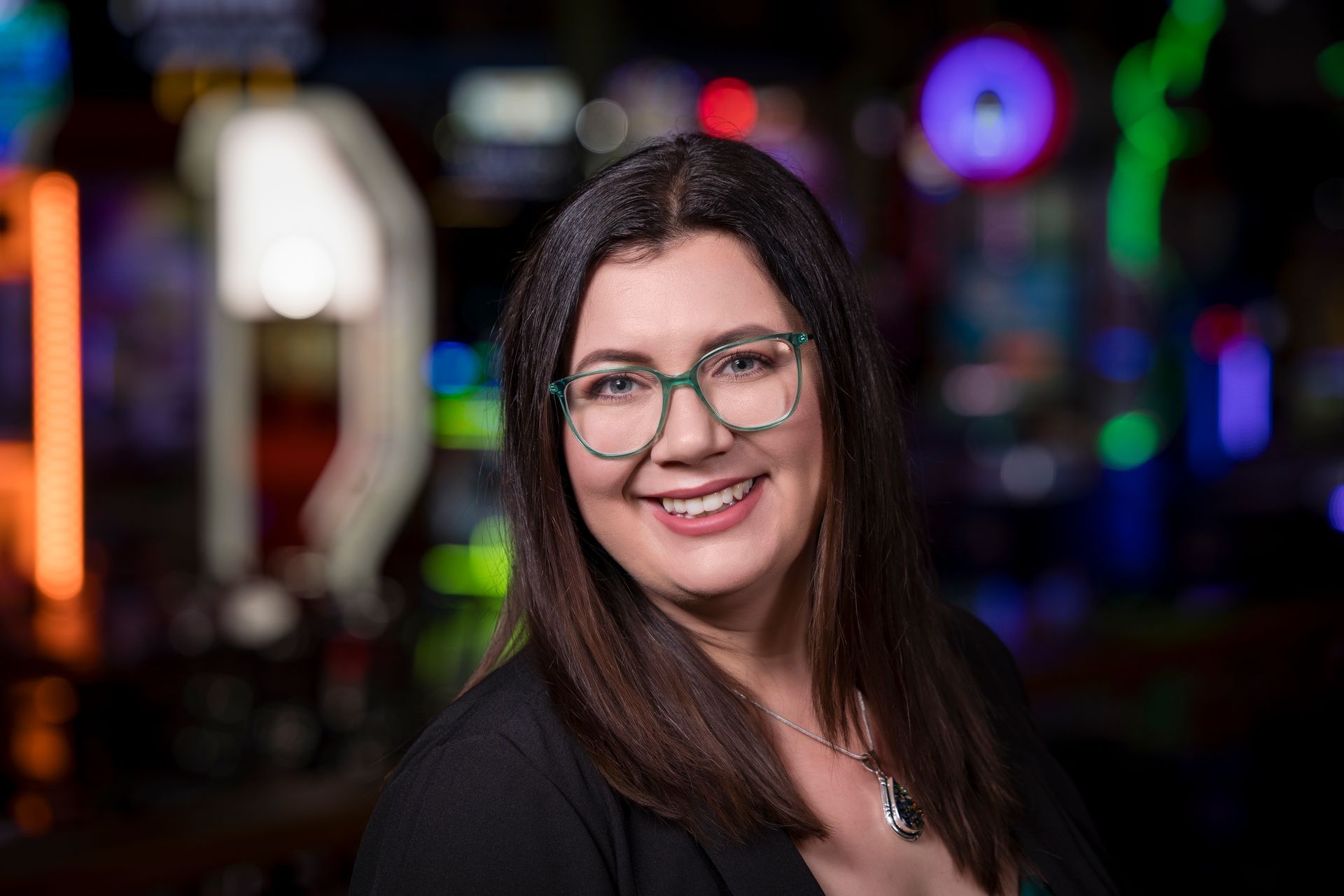 Smiling person with glasses in a dimly lit, colorful background