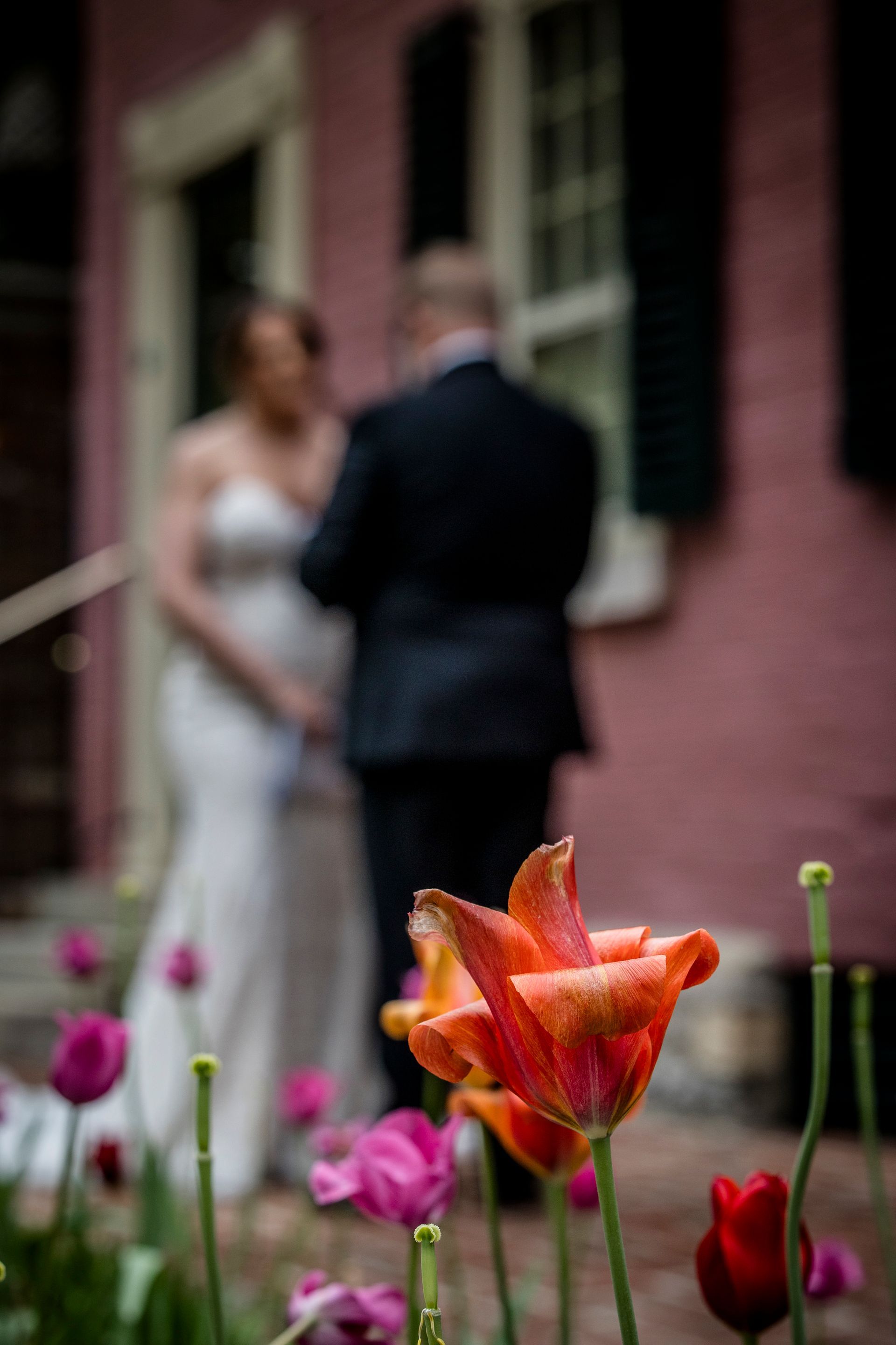 Bride and groom blurred in background, orange flower in sharp focus in foreground