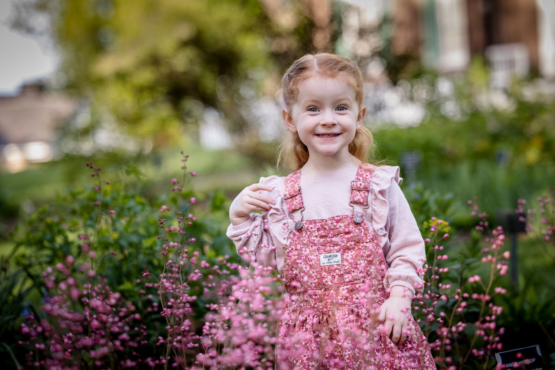 Smiling child in pink dress standing in a flower garden with pink blossoms