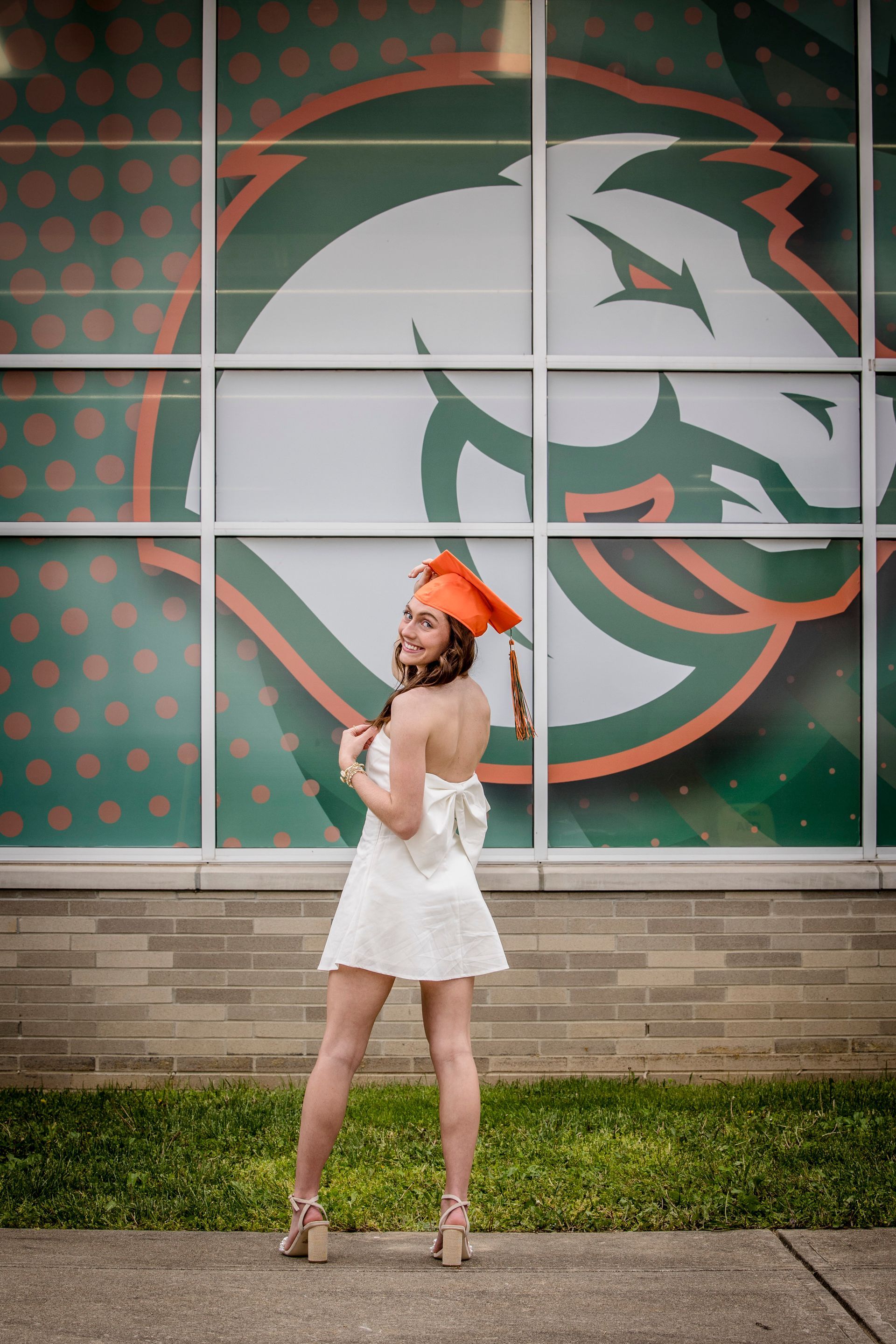 Woman in white dress posing in front of a large horse logo mural, wearing an orange hat.