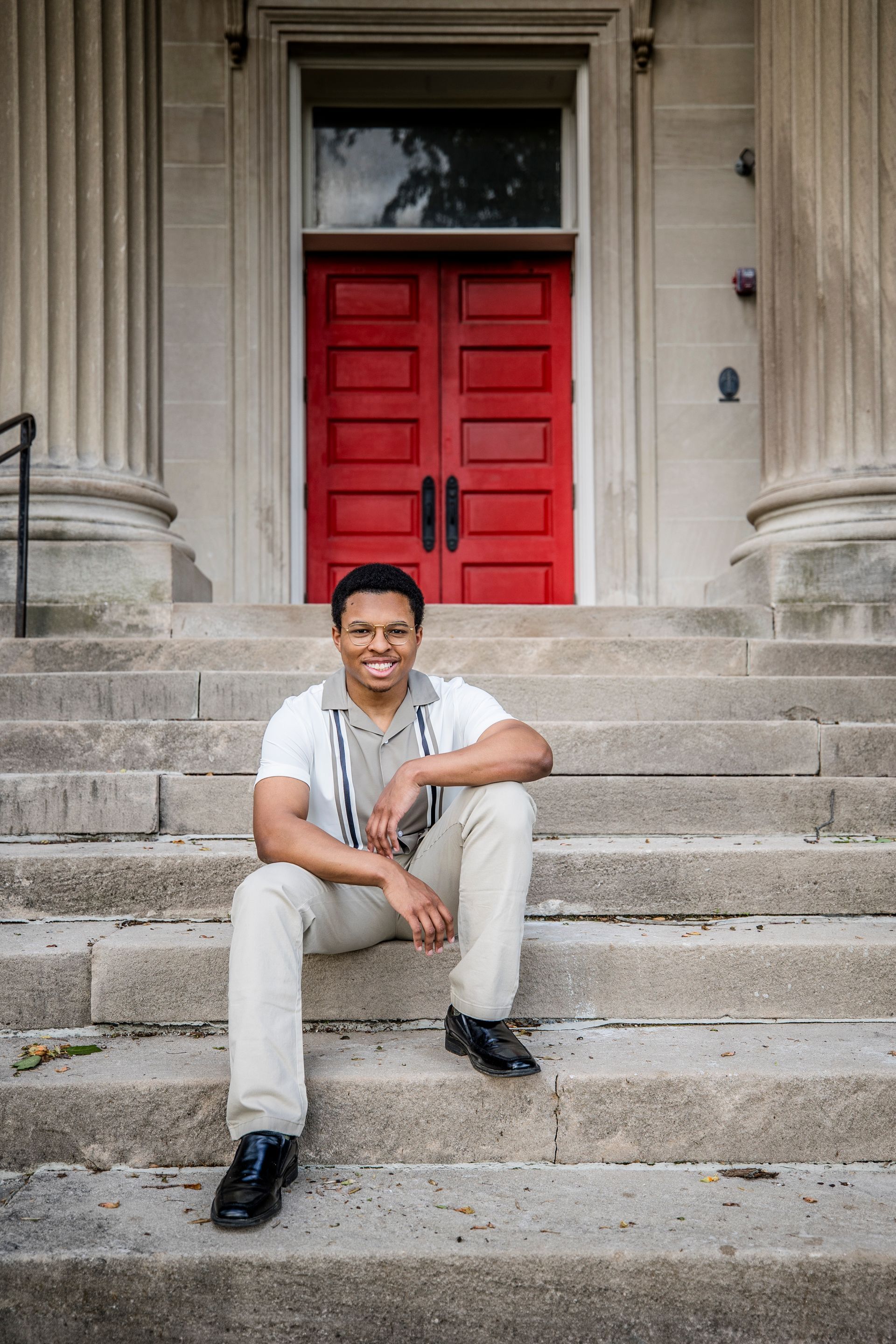 Person sitting on stone steps in front of a red door and columns.