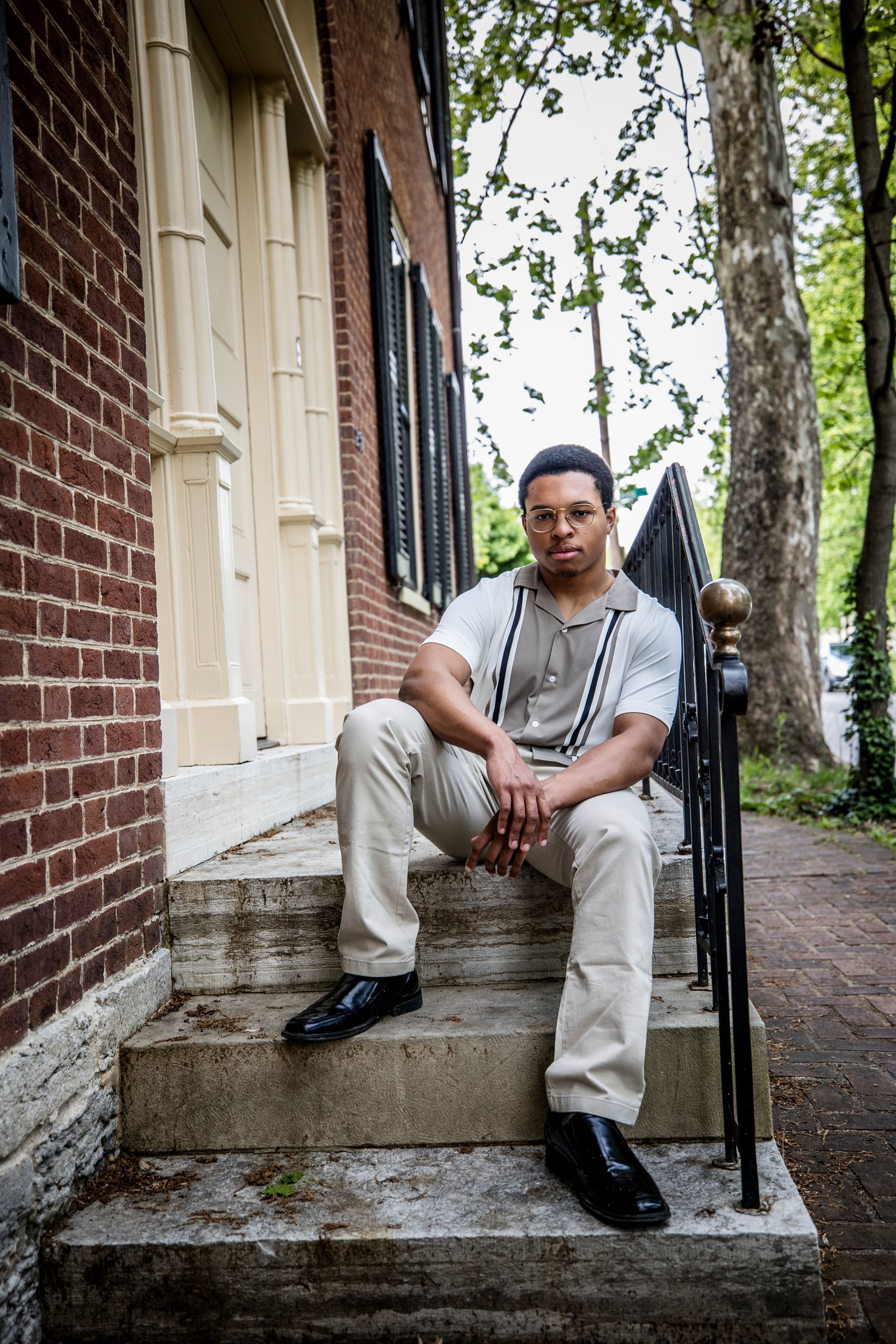 Person seated on stone steps outside a brick building, wearing light clothing and looking at the camera.